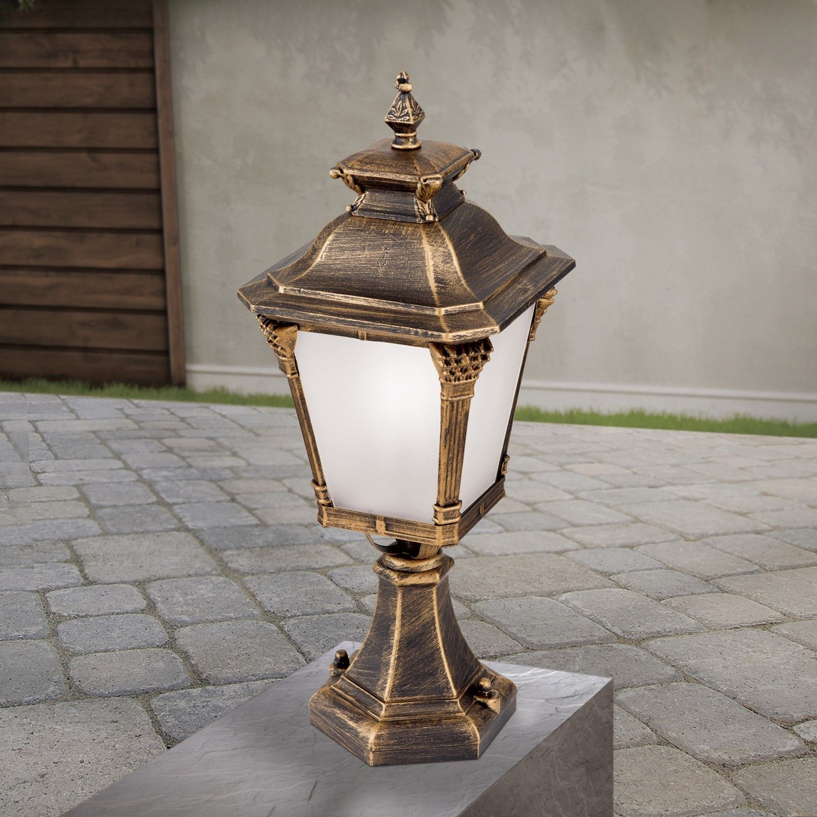 Eine antike goldene Außenlampe auf einem Steinpodest im Garten.
