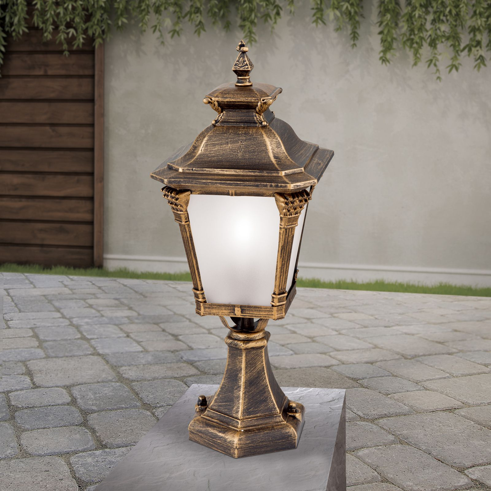 Eine antike, gold-schwarze Gartenlampe steht auf einem Steinpodest vor einer Wand.