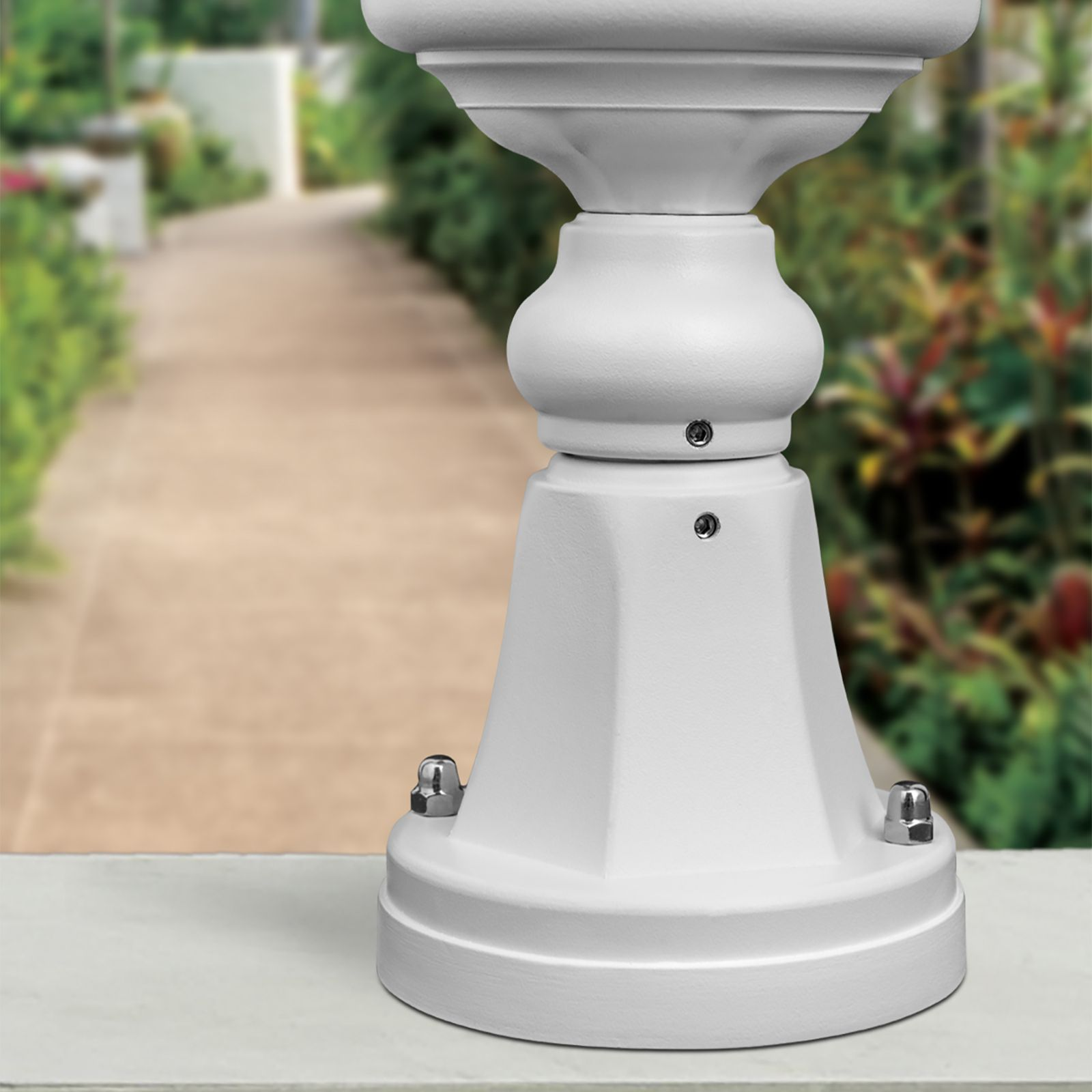 Ein weißer Sockel mit sichtbaren Schrauben im Vordergrund vor einem verschwommenen Gartenweg.