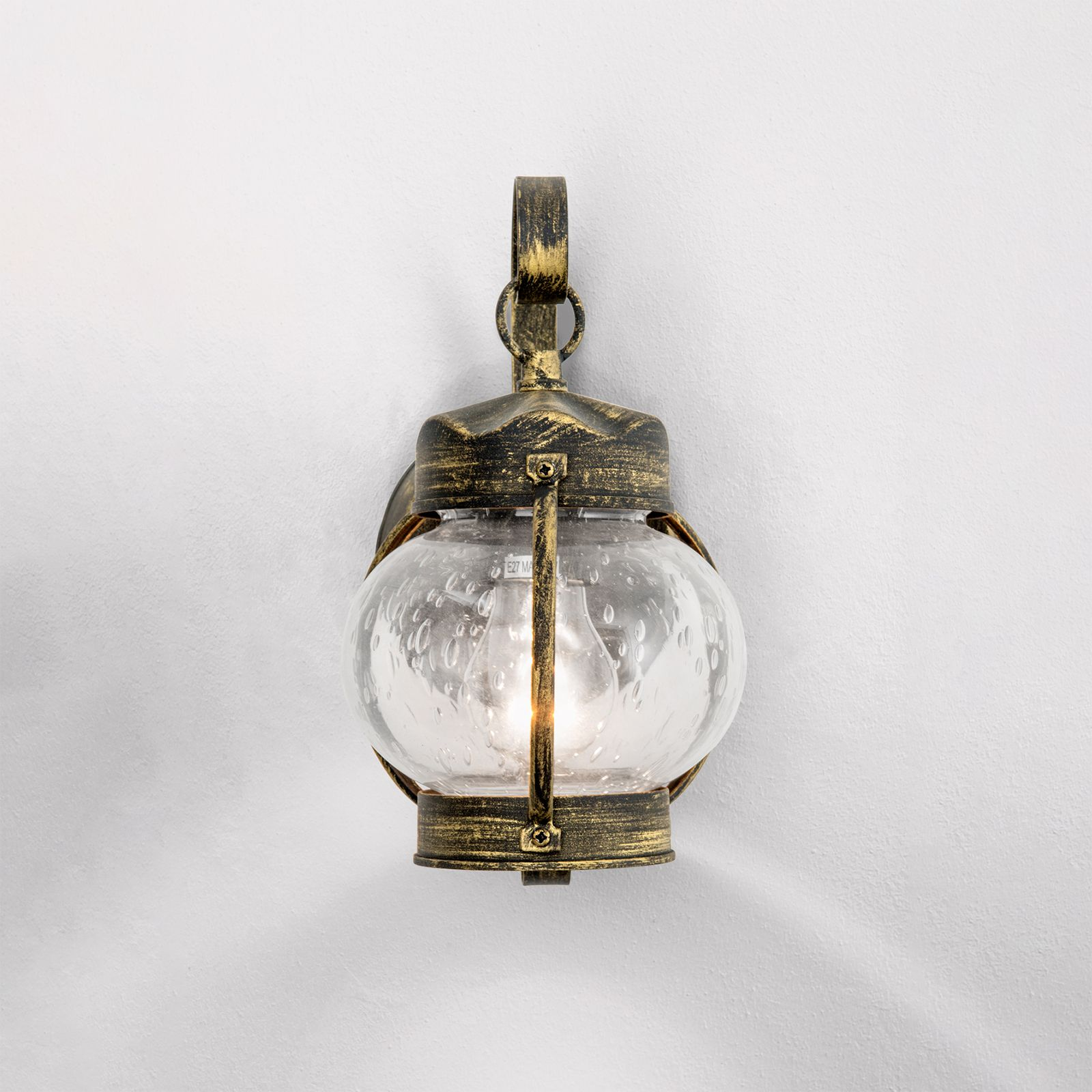 Eine antike goldene Wandleuchte mit bauchigem, strukturiertem Glas an einer weißen Wand.