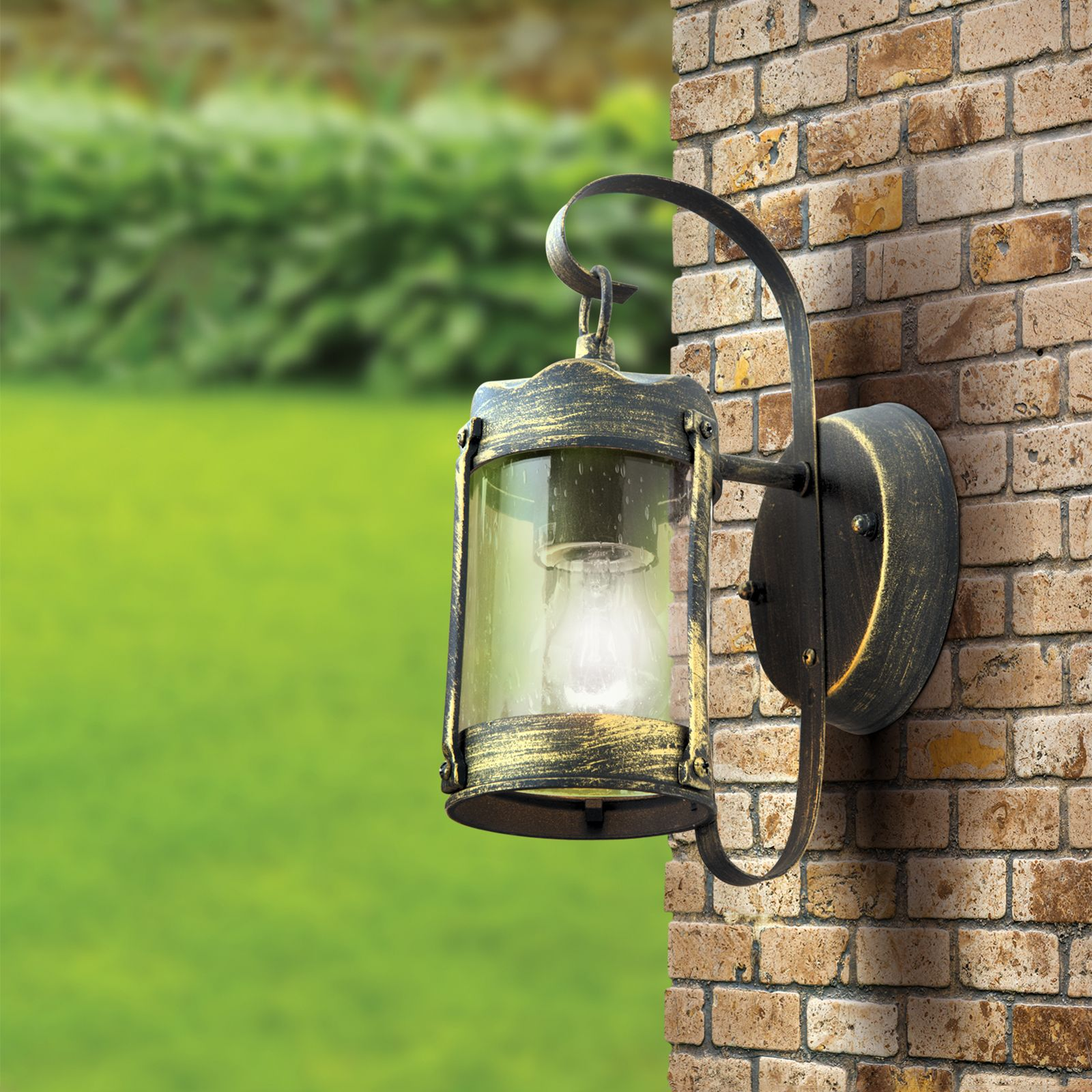 Eine antike schwarze und goldene Wandlampe mit Glaszylinder hängt an einer roten Backsteinmauer im Freien.