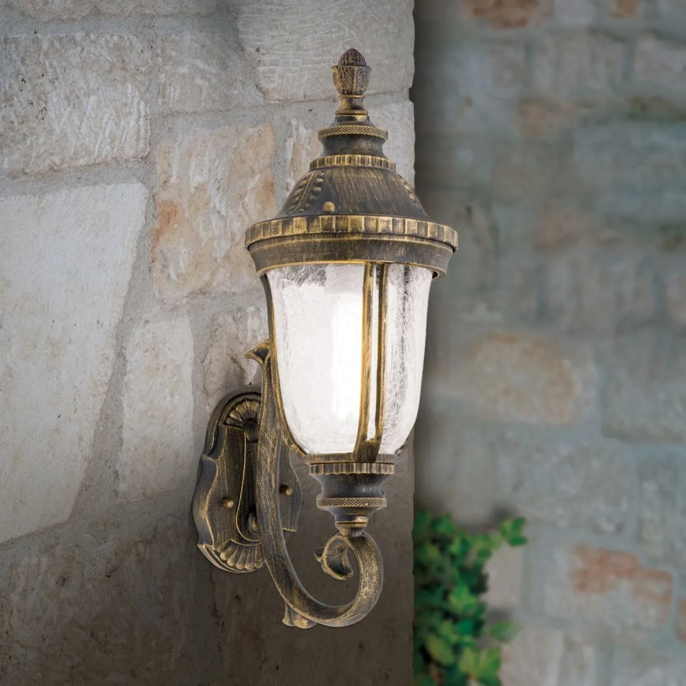 Eine antike Wandleuchte aus Messing mit strukturiertem Glas leuchtet an einer grauen Steinwand.