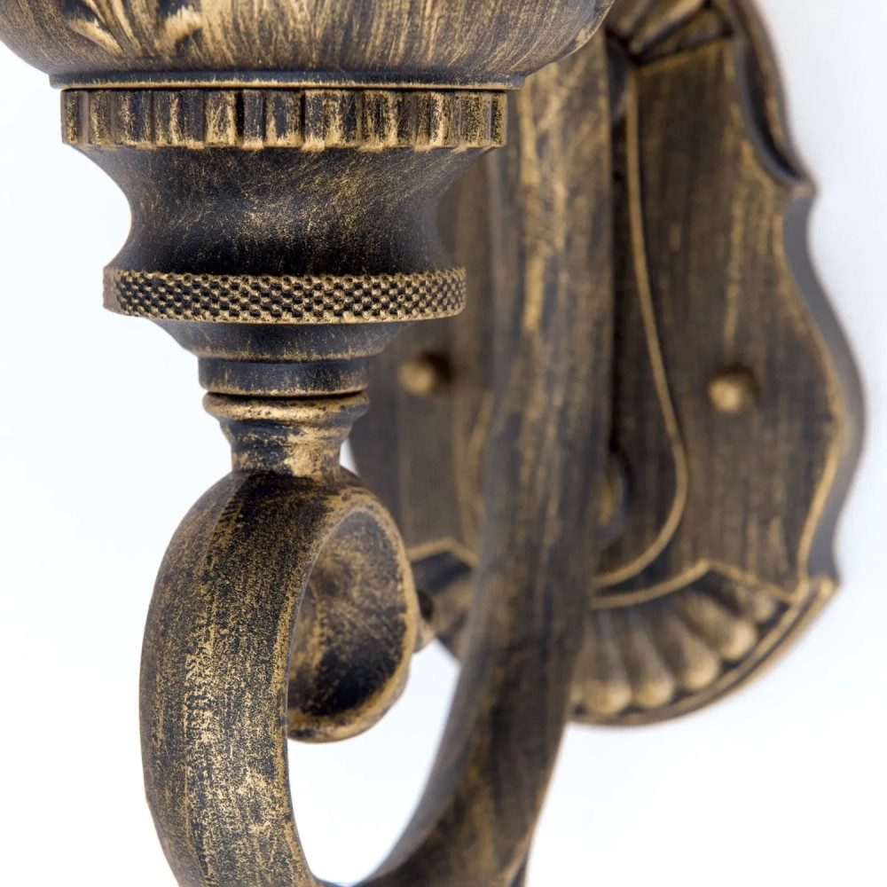 Eine kunstvoll verzierte Wandleuchte in Antikgold und Schwarz vor weißem Hintergrund.