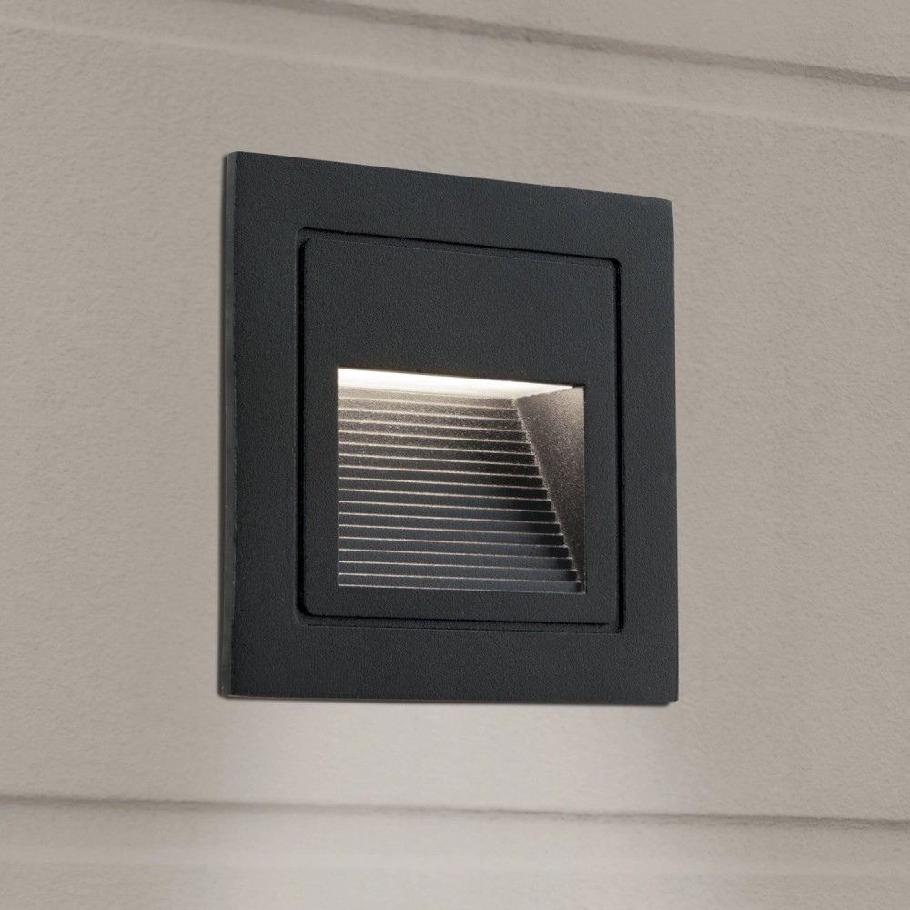 Eine schwarze, quadratische Wandleuchte strahlt sanftes Licht aus einer eingelassenen Öffnung auf eine beige Wand.