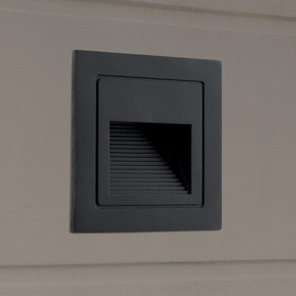 Eine schwarze, quadratische Wandleuchte ist in eine graue Wand eingelassen.