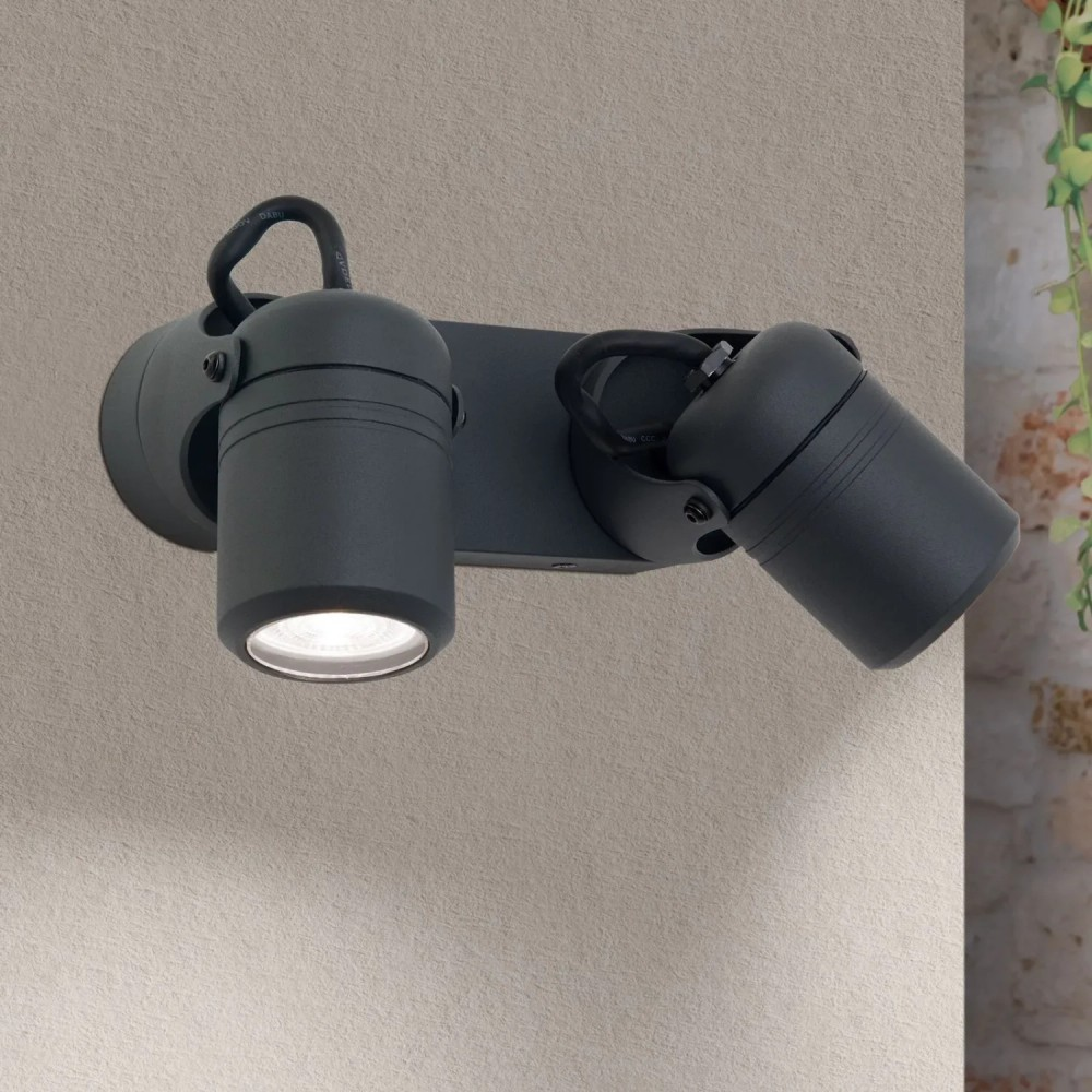 Eine schwarze Doppelwandleuchte mit verstellbaren Spots ist an einer hellen Wand montiert; ein Spot ist eingeschaltet.