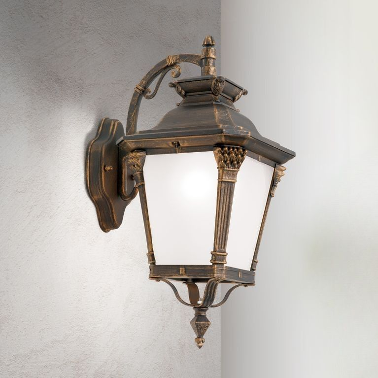 Eine antike schwarze Wandleuchte mit weißem Glas und goldenen Akzenten an einer grauen Wand.