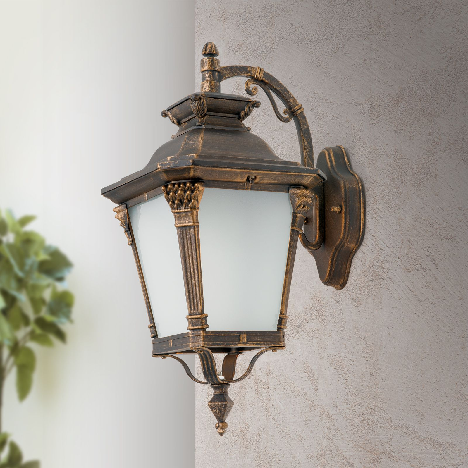 Eine verzierte, dunkle Outdoor-Wandlaterne aus Bronze mit Milchglasscheiben an einer strukturierten grauen Wand.