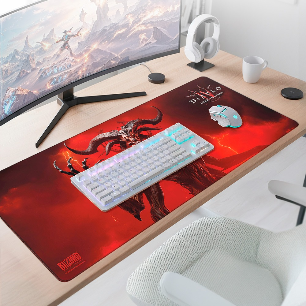 Ein Gaming-Schreibtisch mit Monitor, einer Teufel-Mausmatte, weißer Tastatur, Maus, Kopfhörern und einer Tasse.