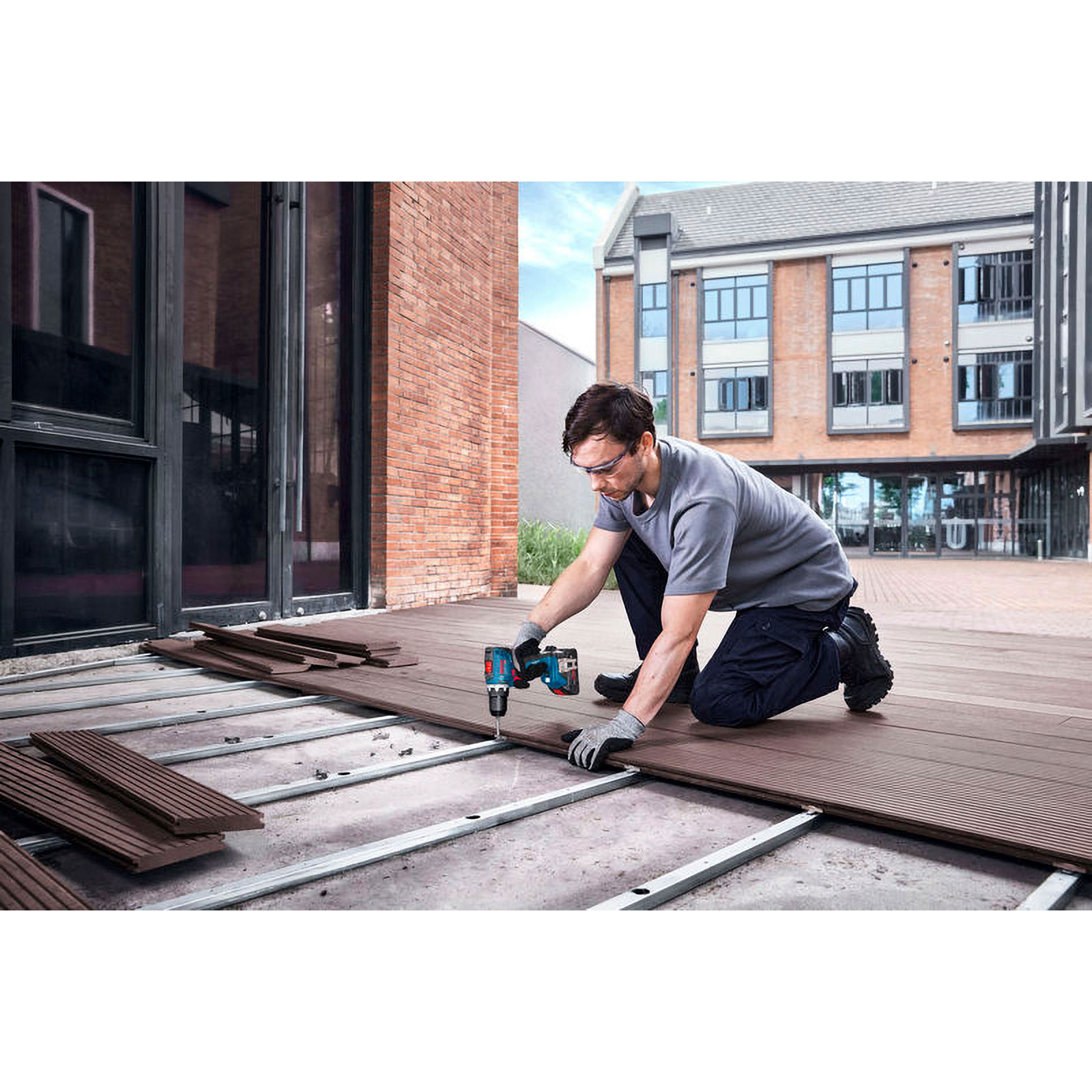 Ein Arbeiter baut draußen eine Holzterrasse mit einer Bohrmaschine.