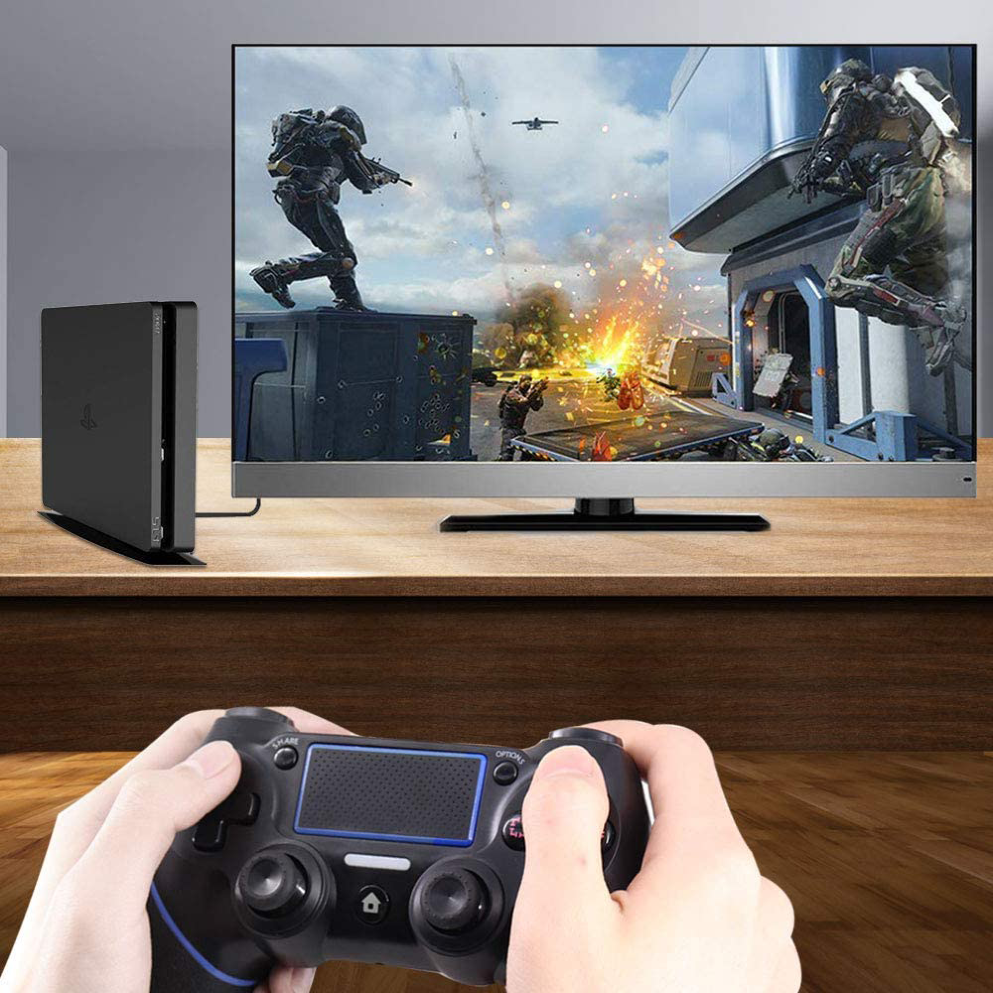 Eine Person spielt mit einem schwarzen Controller ein Videospiel auf einem Fernseher, daneben steht eine Konsole.