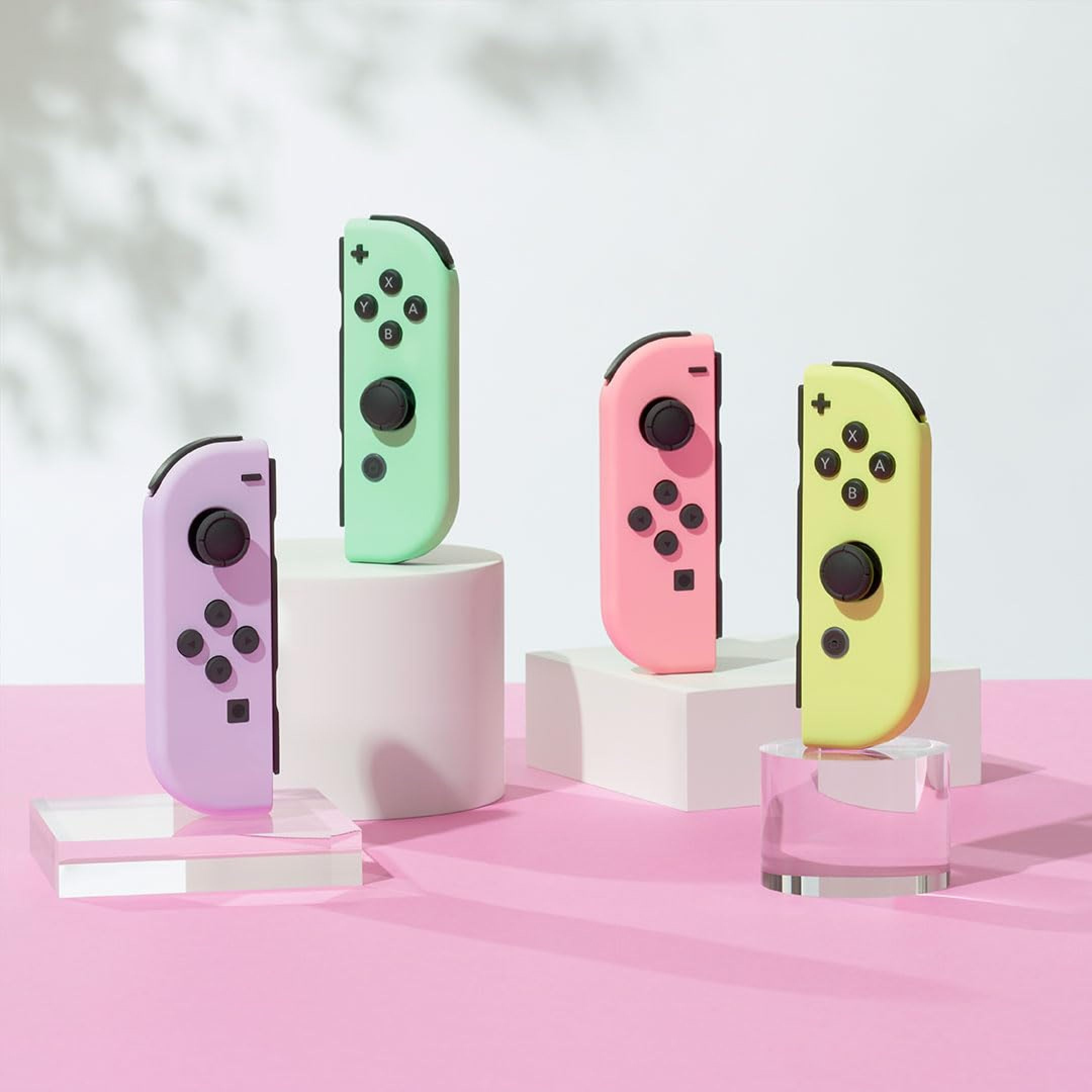 Vier bunte Nintendo Switch Joy-Con Controller stehen auf kleinen Podesten vor einem hellen Hintergrund.