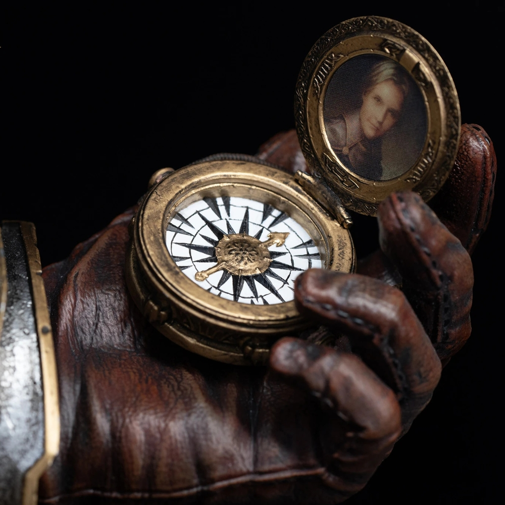Eine behandschuhte Hand hält einen verzierten Goldkompass mit einem Porträt im offenen Deckel vor dunklem Hintergrund.