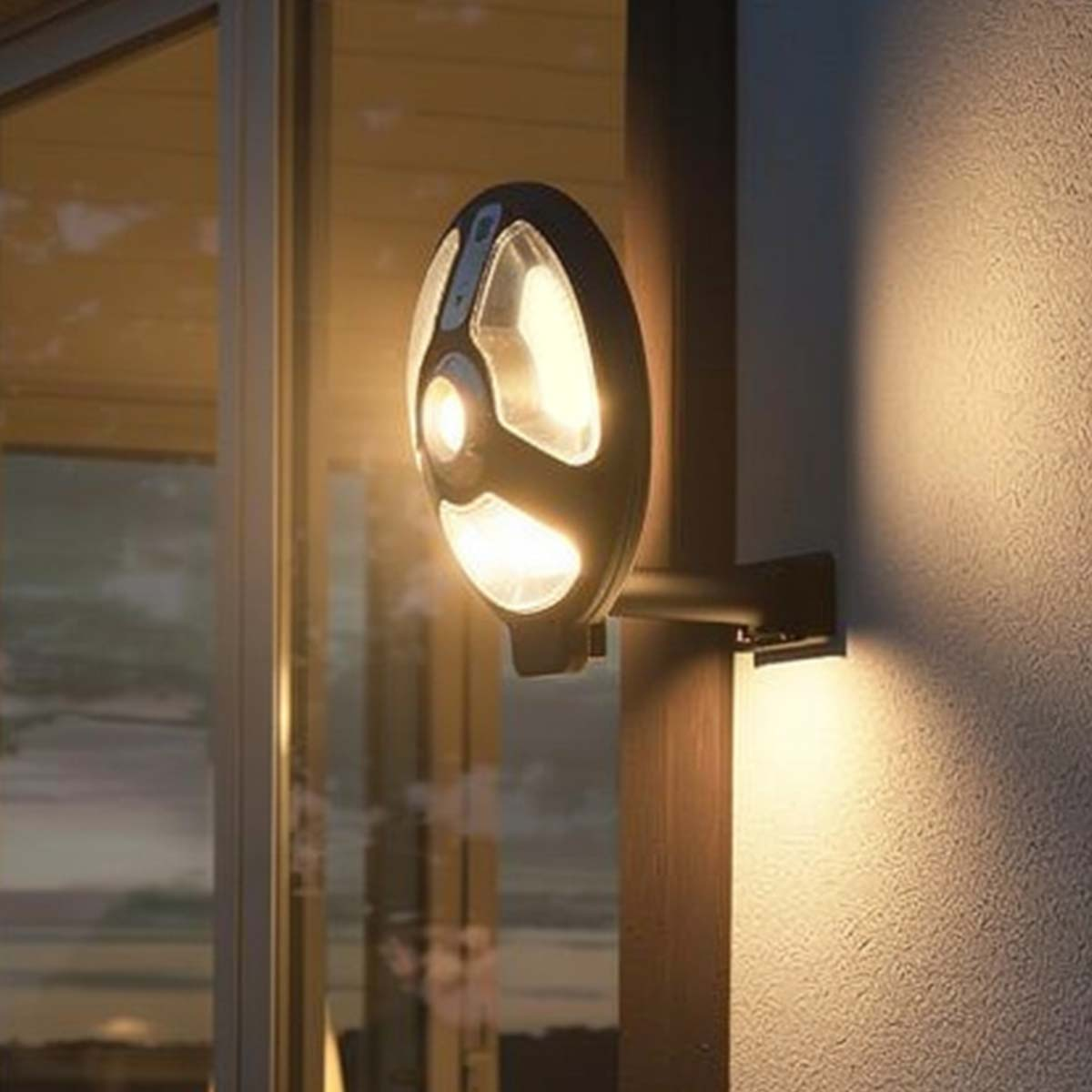 Eine moderne schwarze Außenwandleuchte an einem Glasfenster, die warmes Licht wirft.