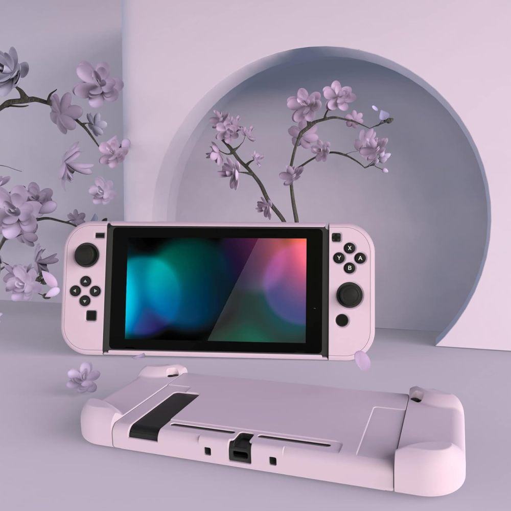 Eine pastellrosa Handheld-Spielkonsole vor einer runden Nische und Zweigen mit lila Blüten.
