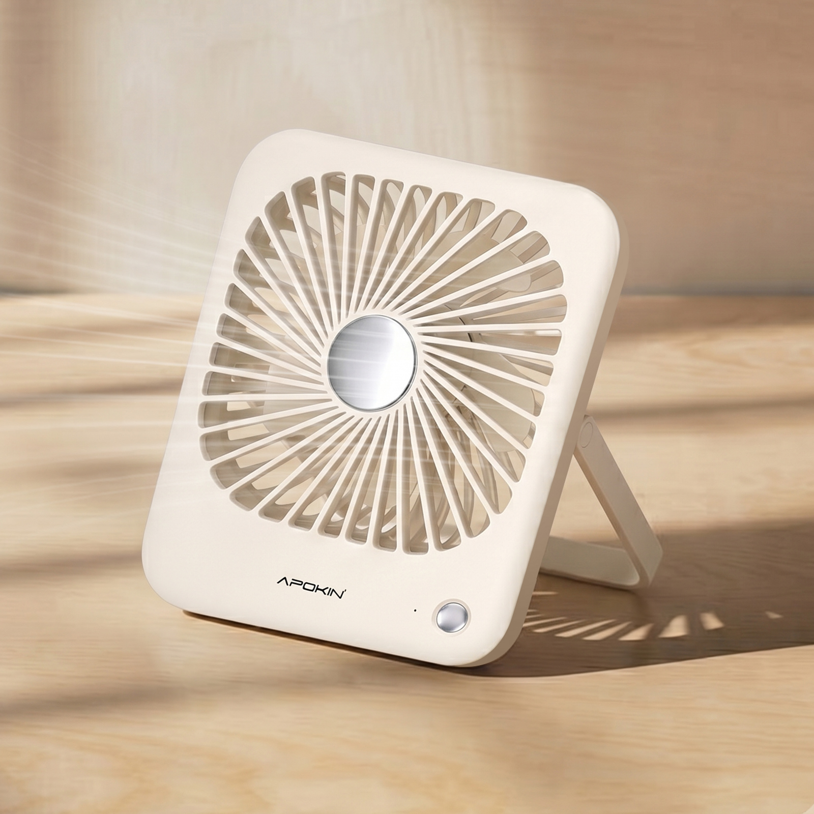 Ein beiger, quadratischer Tischventilator mit silbernem Mittelkreis steht auf Holz und bläst Luft.