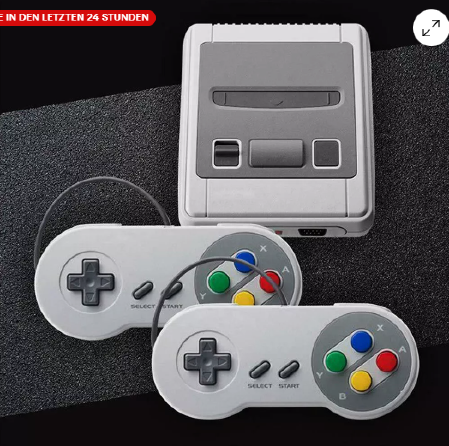 Eine graue Retro-Spielkonsole mit zwei passenden Controllern auf dunkler, strukturierter Oberfläche.