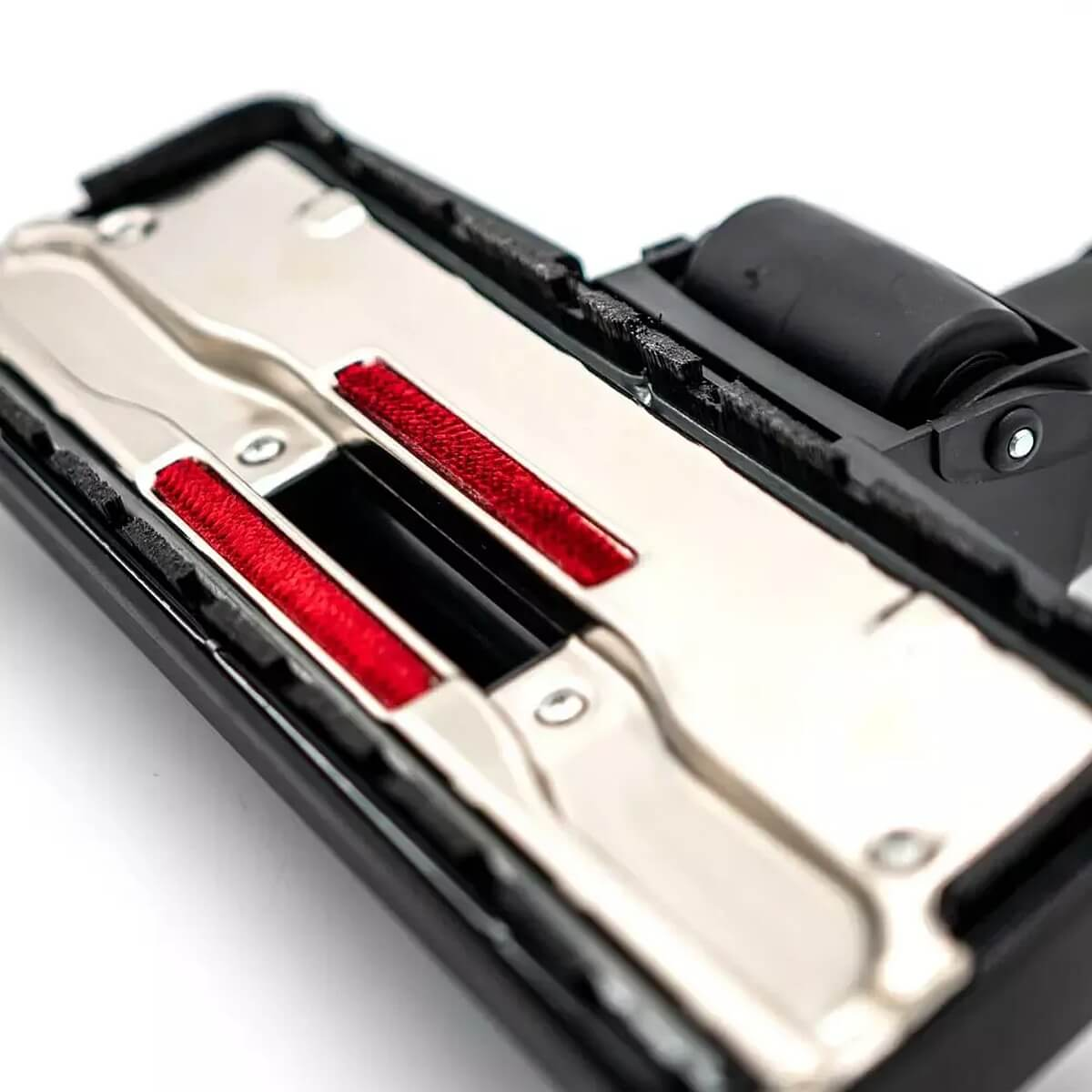 Vue de dessous d'un accessoire d'aspirateur avec plaque métallique et bandes rouges.