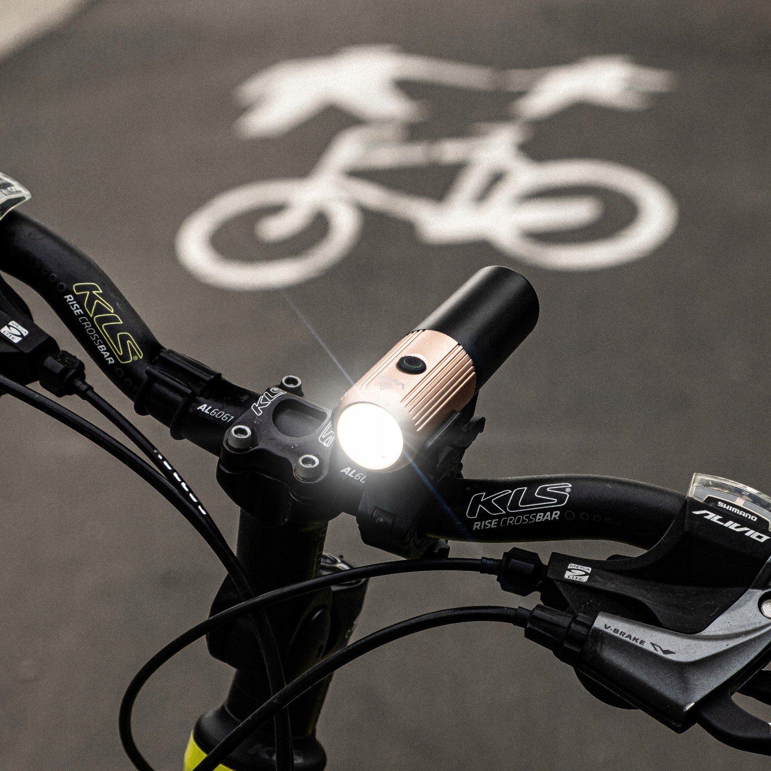 Fahrradlenker mit eingeschaltetem Scheinwerfer vor einem Fahrradwegsymbol auf dem Boden.