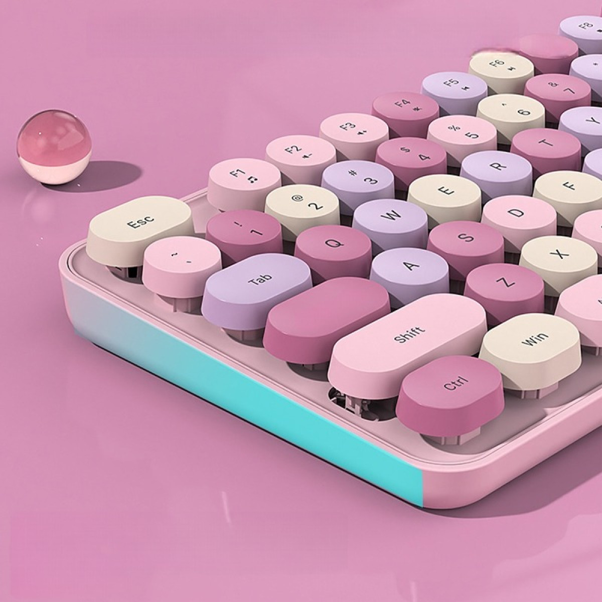 Eine pastellrosa und blaue kabellose Tastatur mit runden Tasten im Schreibmaschinenstil liegt auf einer rosa Oberfläche.