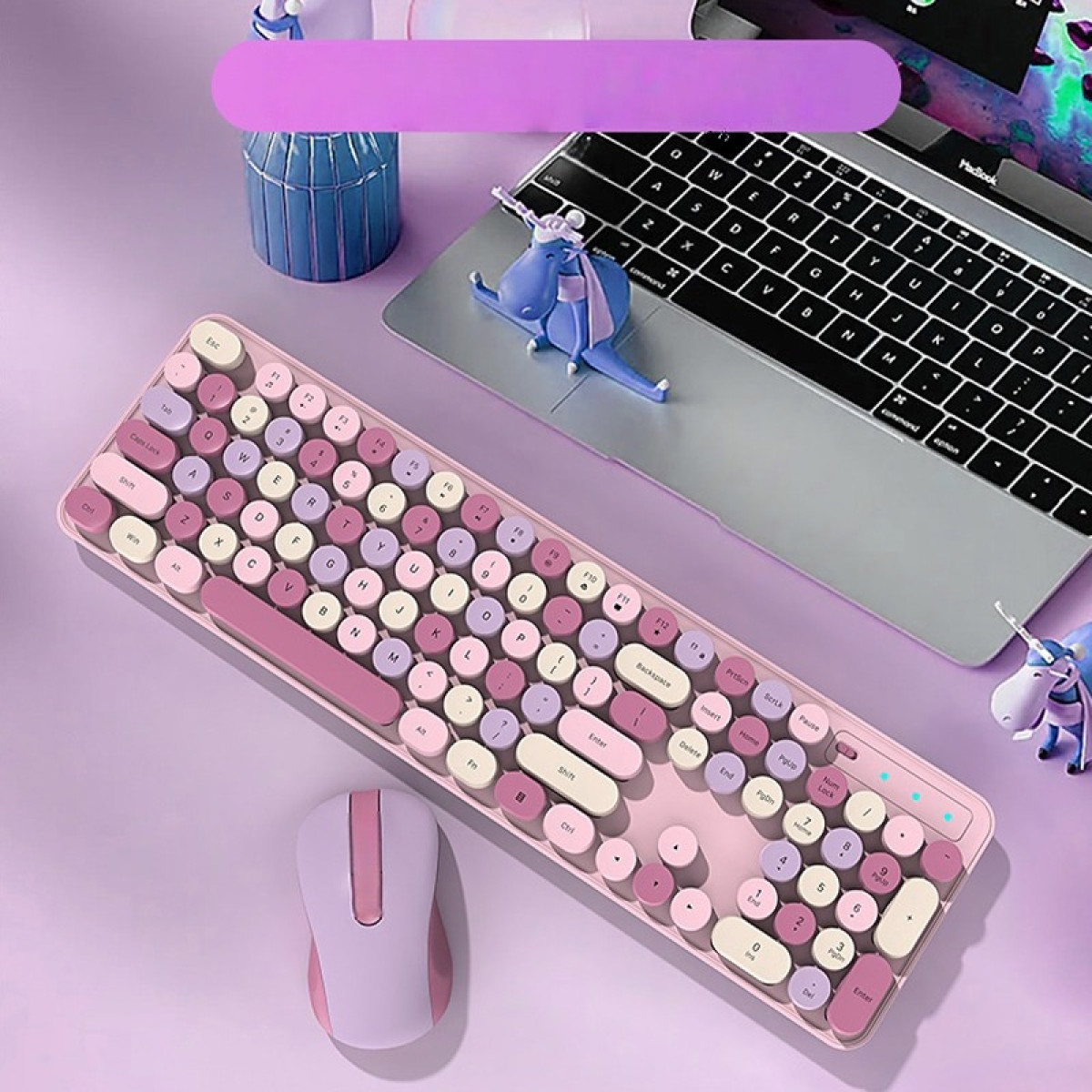 Ein lilafarbener Schreibtisch mit einer rosa-lilanen Retro-Tastatur, passender Maus, Laptop und kleinen Einhornfiguren.