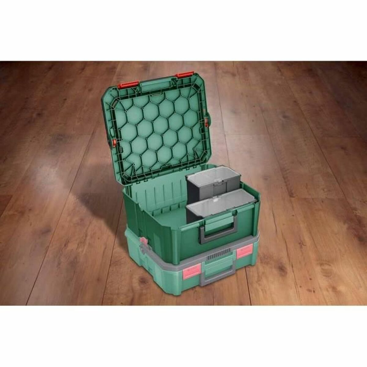 Eine offene grüne Aufbewahrungsbox mit kleinen grauen Inneneinsätzen auf einer anderen Box auf Holzboden.