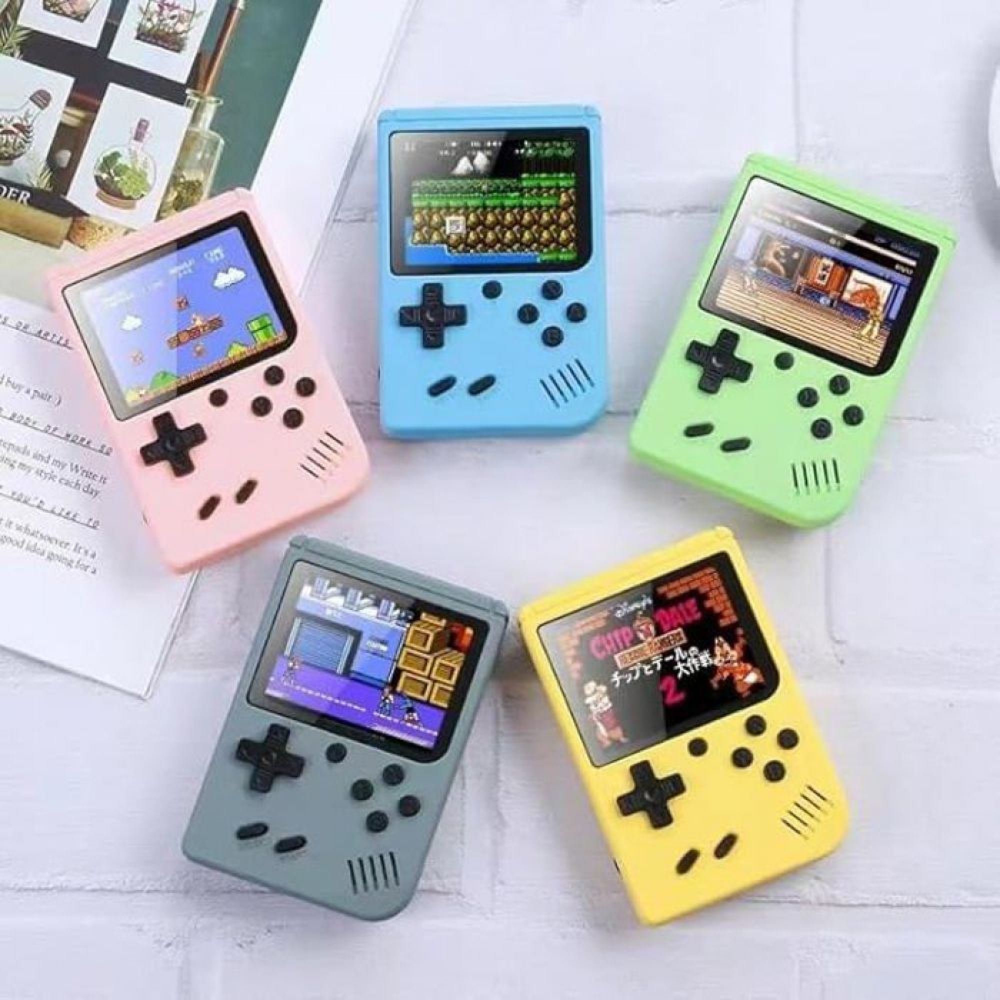 Vier bunte Handheld-Konsolen mit verschiedenen angezeigten Videospielen liegen auf einer weißen Oberfläche.