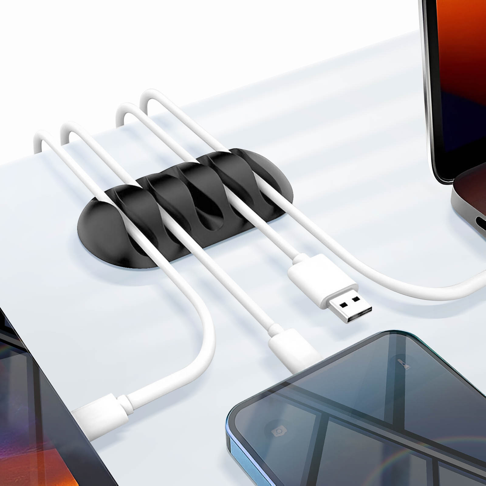 Ein schwarzer Kabelorganisator aus Silikon auf einem weißen Schreibtisch hält vier weiße Ladekabel.