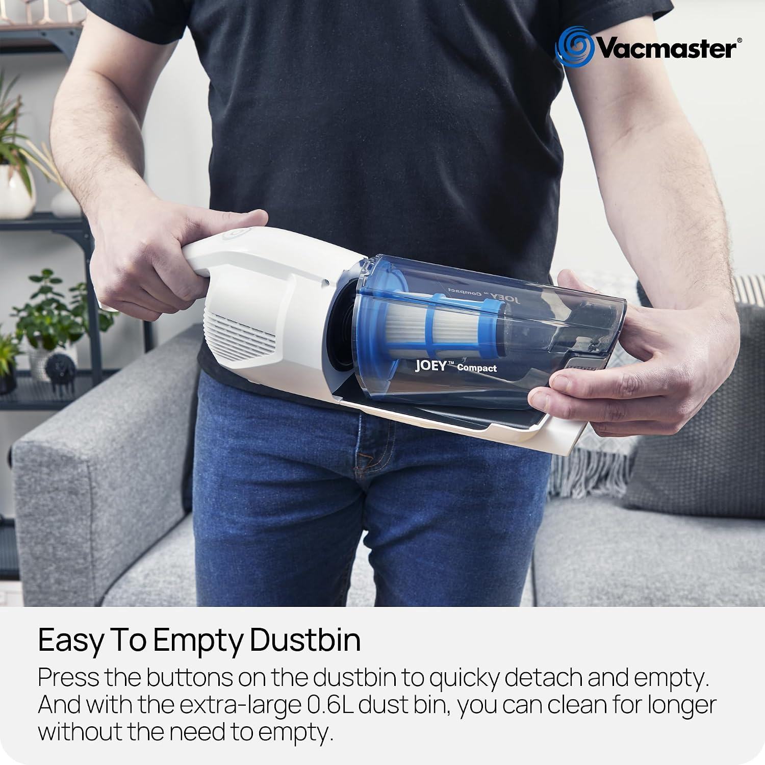 Eine Person hält einen weiß-blauen Vacmaster Joey Compact Handstaubsauger über ein Sofa.