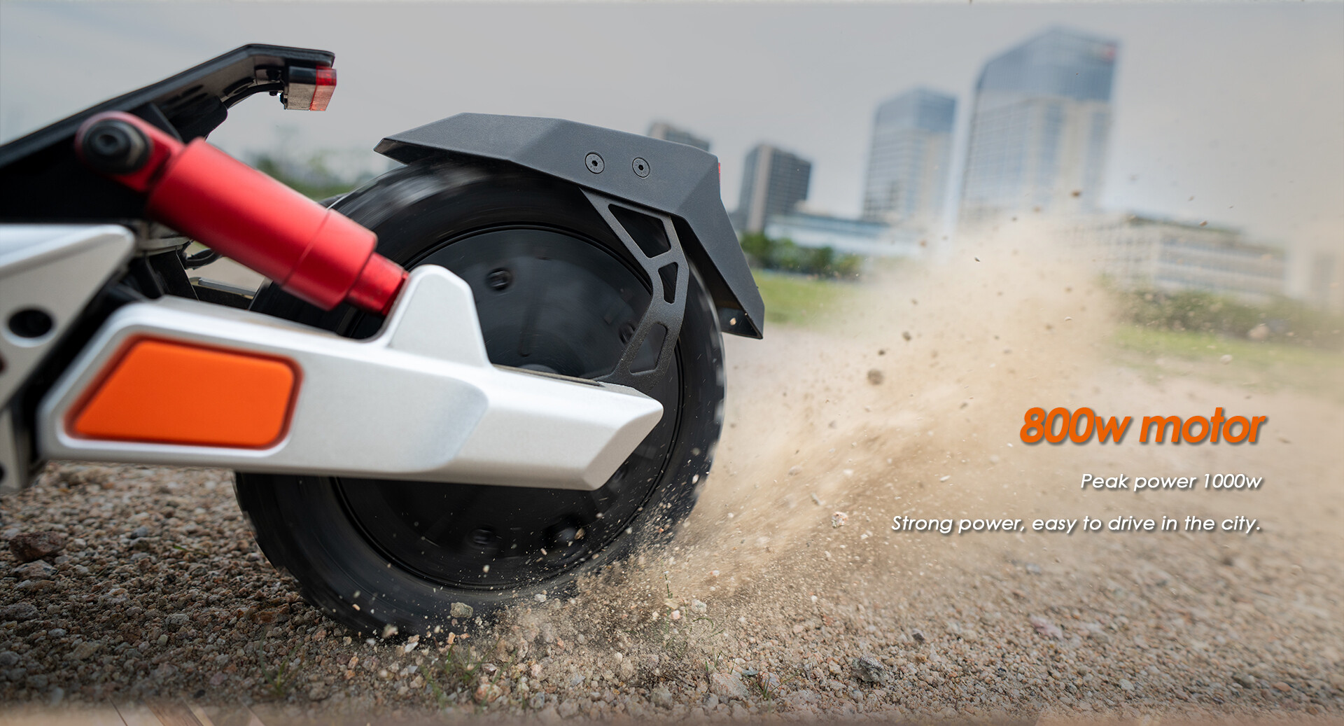 Un monopattino elettrico solleva ghiaia, con una città sullo sfondo e il testo su un motore da 800w.