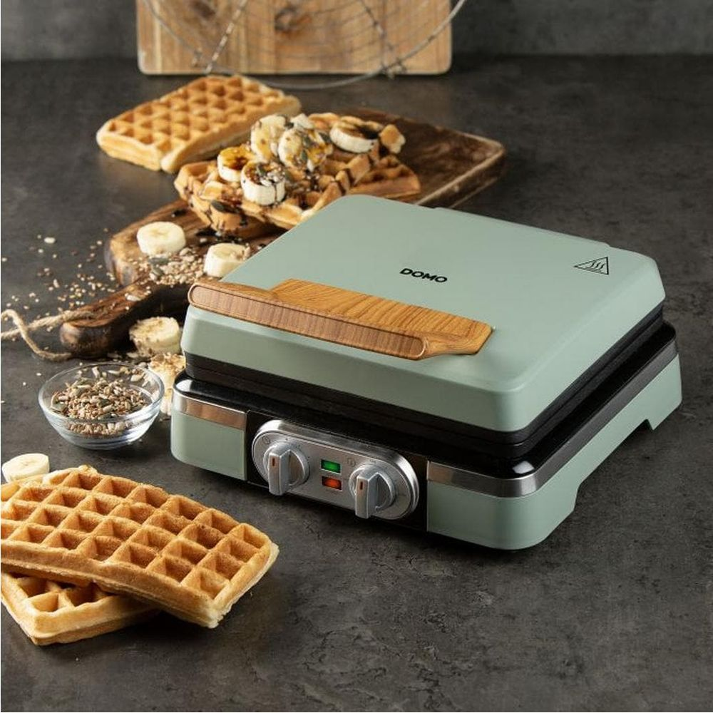 Una piastra per waffle verde menta su superficie scura con waffle e fette di banana.