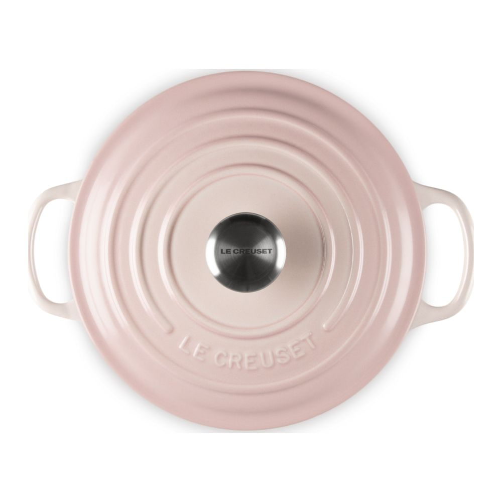 Vue de dessus d'une cocotte Le Creuset ronde rose clair avec un bouton métallique et des poignées sur fond blanc.