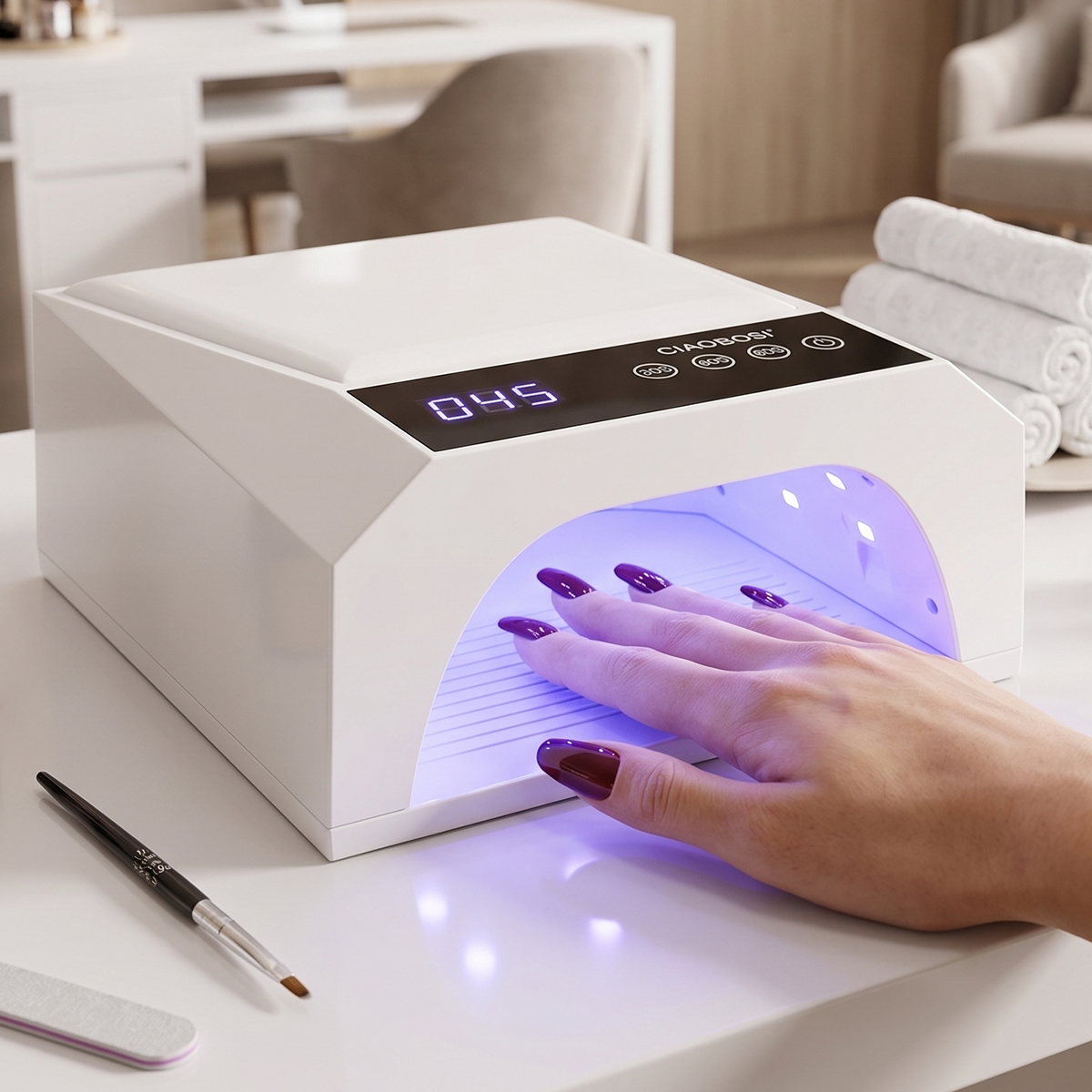 Eine Hand mit dunkelroten Nägeln im Inneren einer weißen UV-Nagellampe auf einem Tisch.