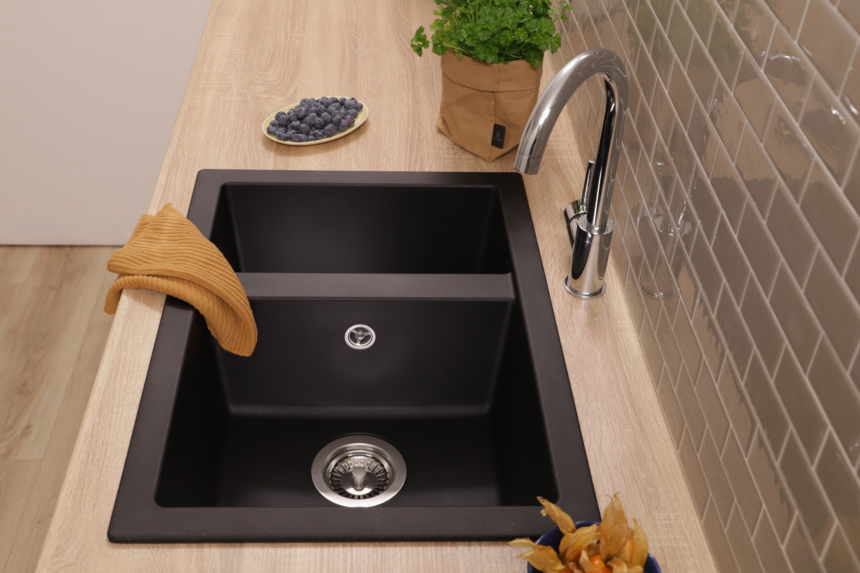 Ein schwarzes Doppelwaschbecken mit Chromarmatur auf Holzarbeitsplatte, Spültuch, Blaubeerschale und Pflanze.