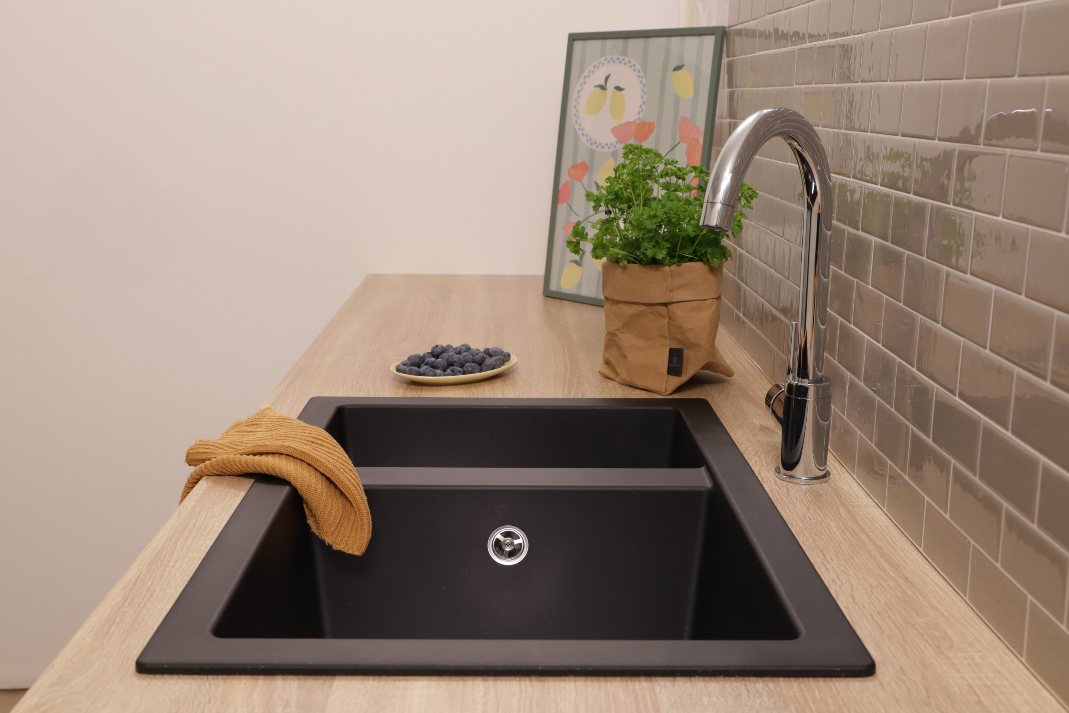 Schwarzes Doppelbecken in Holzarbeitsplatte, verchromter Wasserhahn, Beeren, Papiertüte mit Pflanze und gerahmtes Bild.
