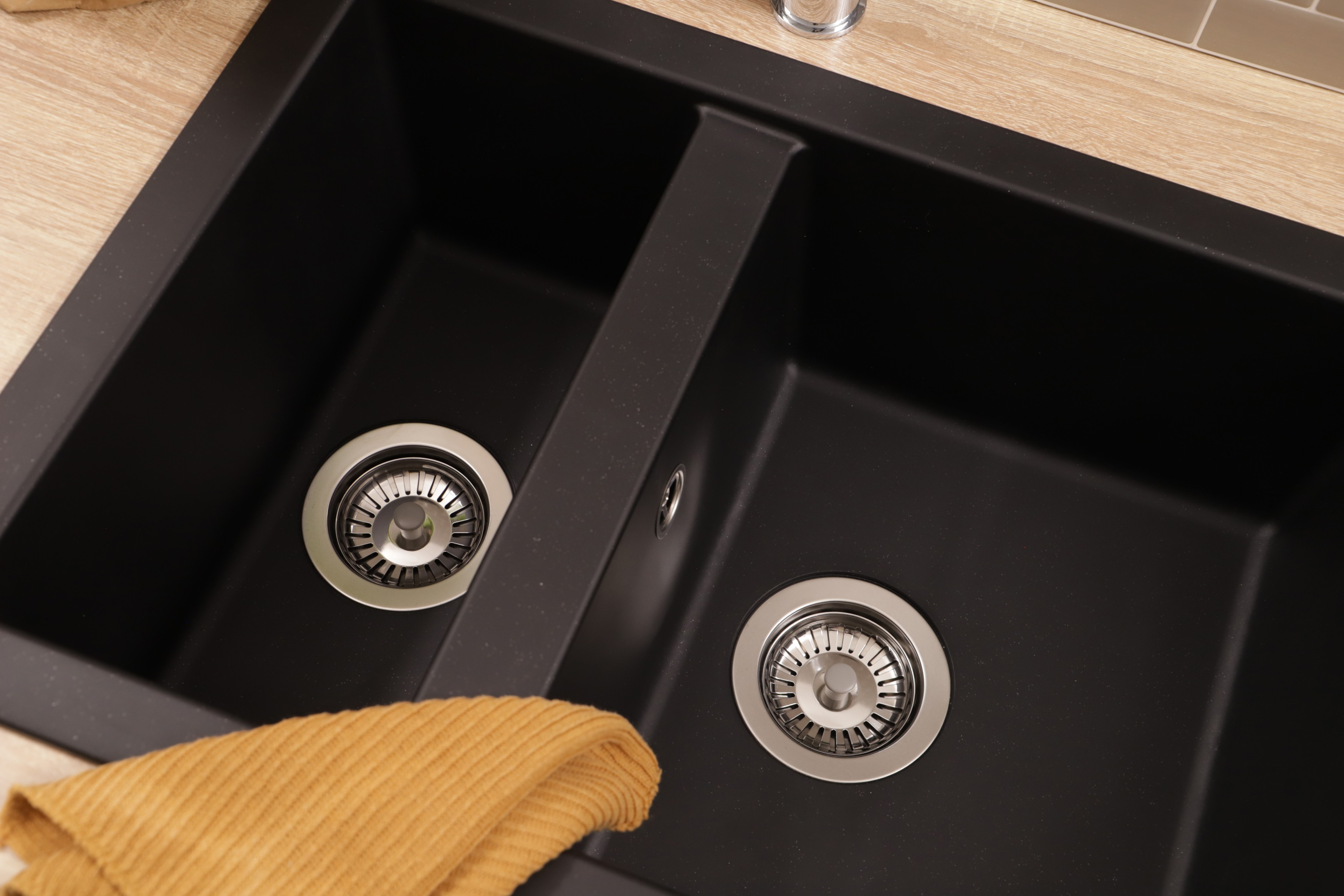 Ein doppeltes schwarzes Spülbecken mit Metallabflüssen und einem gelben Handtuch in einer Holzküche.