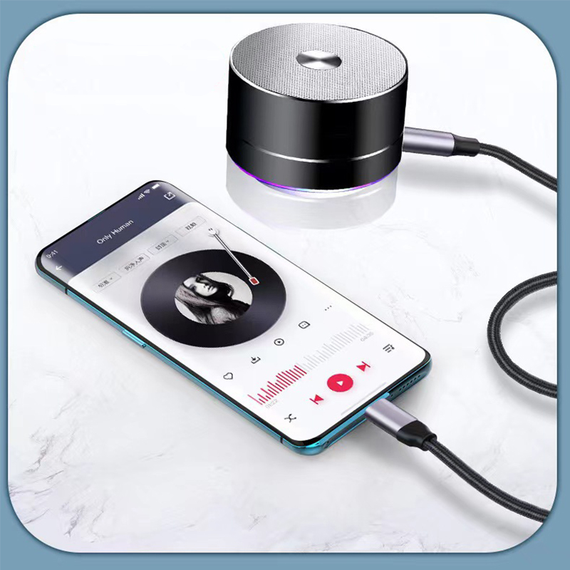 Ein zylindrischer Bluetooth-Lautsprecher ist per Kabel mit einem Smartphone verbunden, auf dem ein Musikplayer läuft.