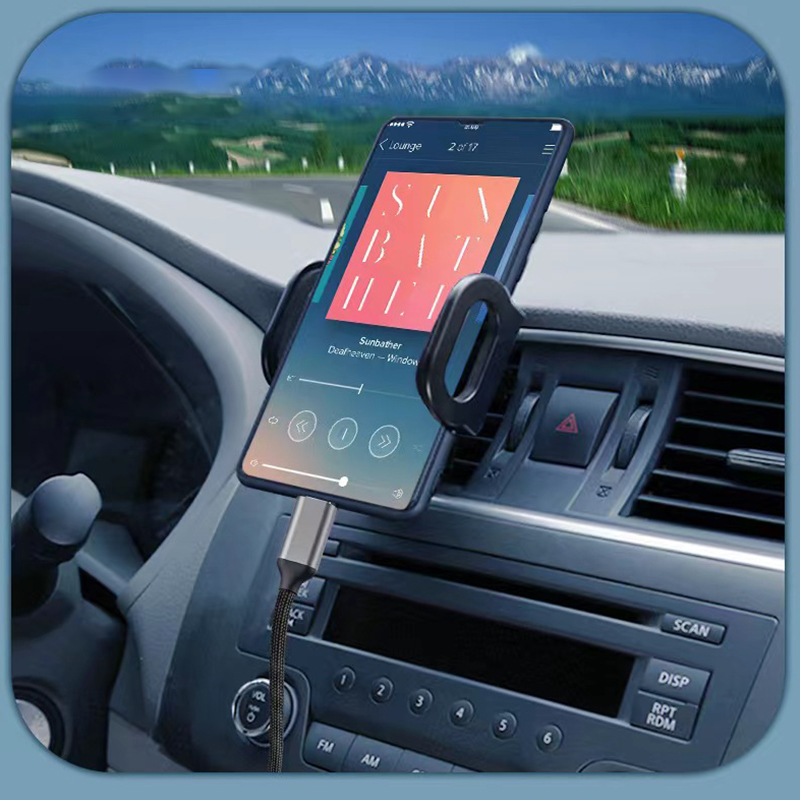 Ein Smartphone mit Musikplayer in einer Autohalterung, verbunden mit einem Ladekabel, vor einer Landschaft.
