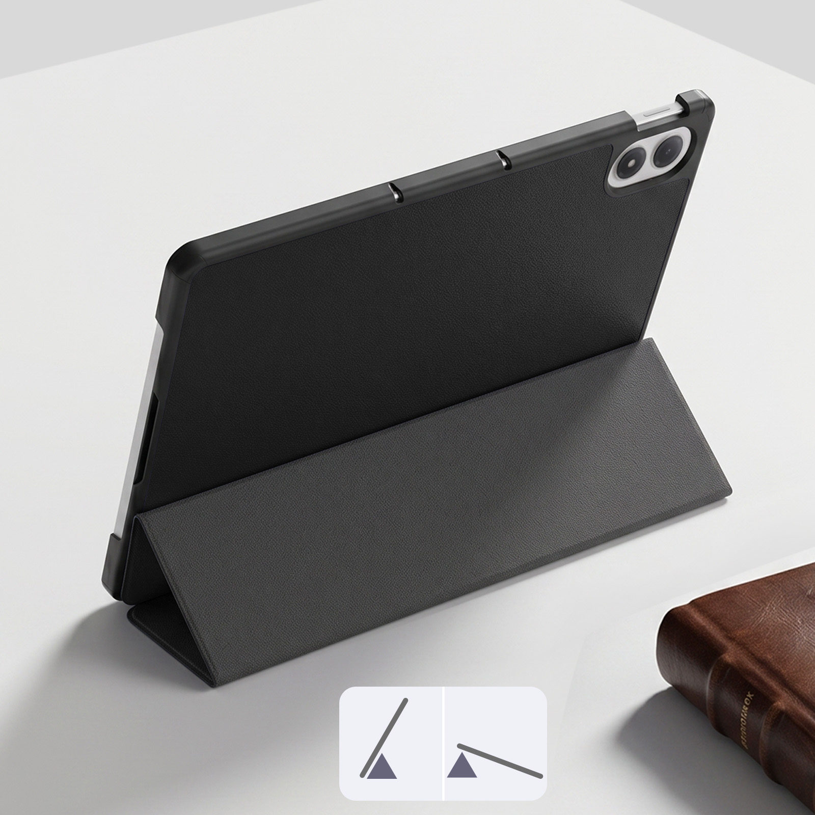 Ein graues Tablet mit Schutzhülle steht schräg auf einer weißen Oberfläche neben einem braunen Buch.