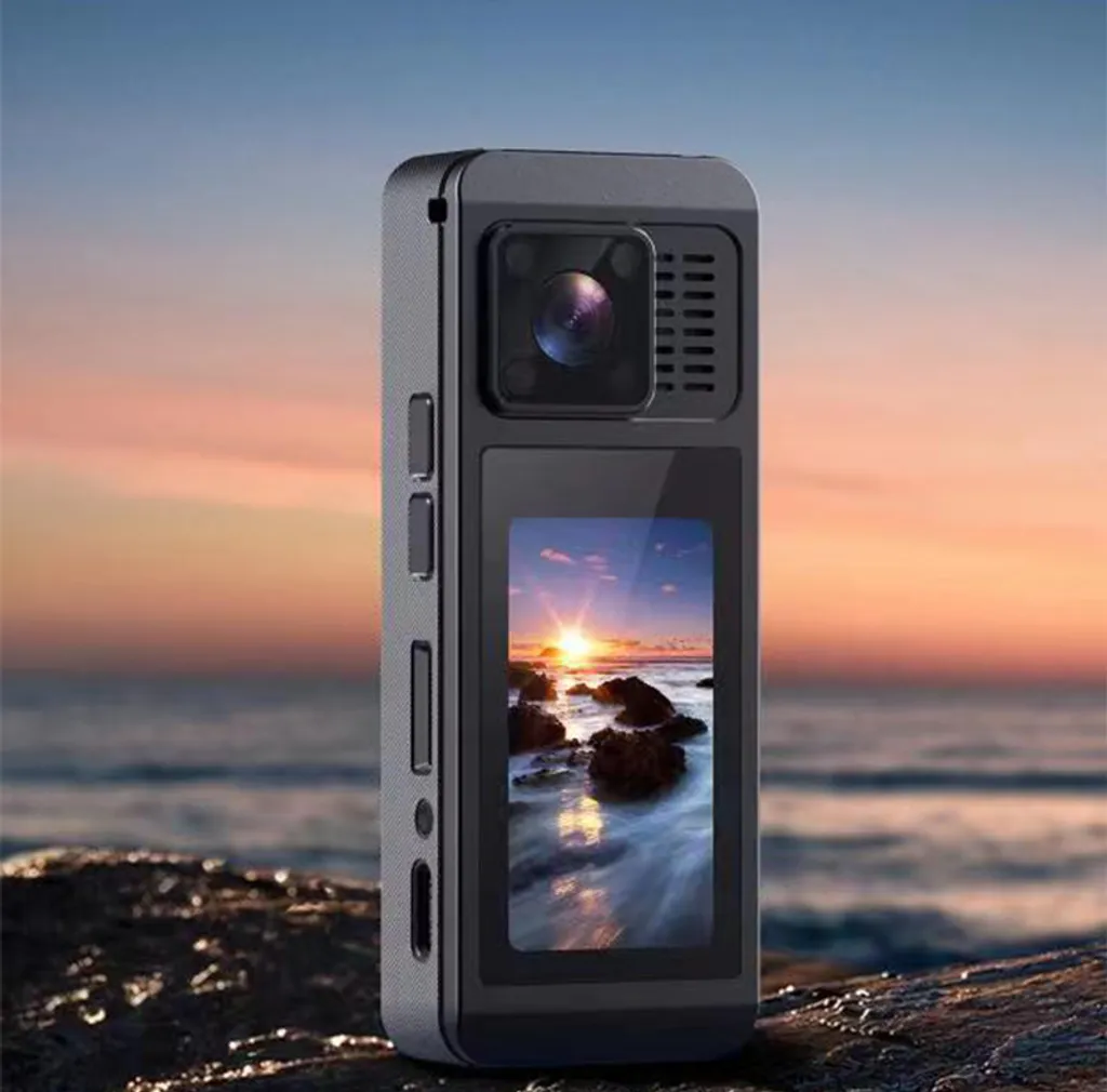 Eine graue Action-Kamera steht auf einem felsigen Strand, während im Hintergrund ein Sonnenuntergang am Meer zu sehen ist.
