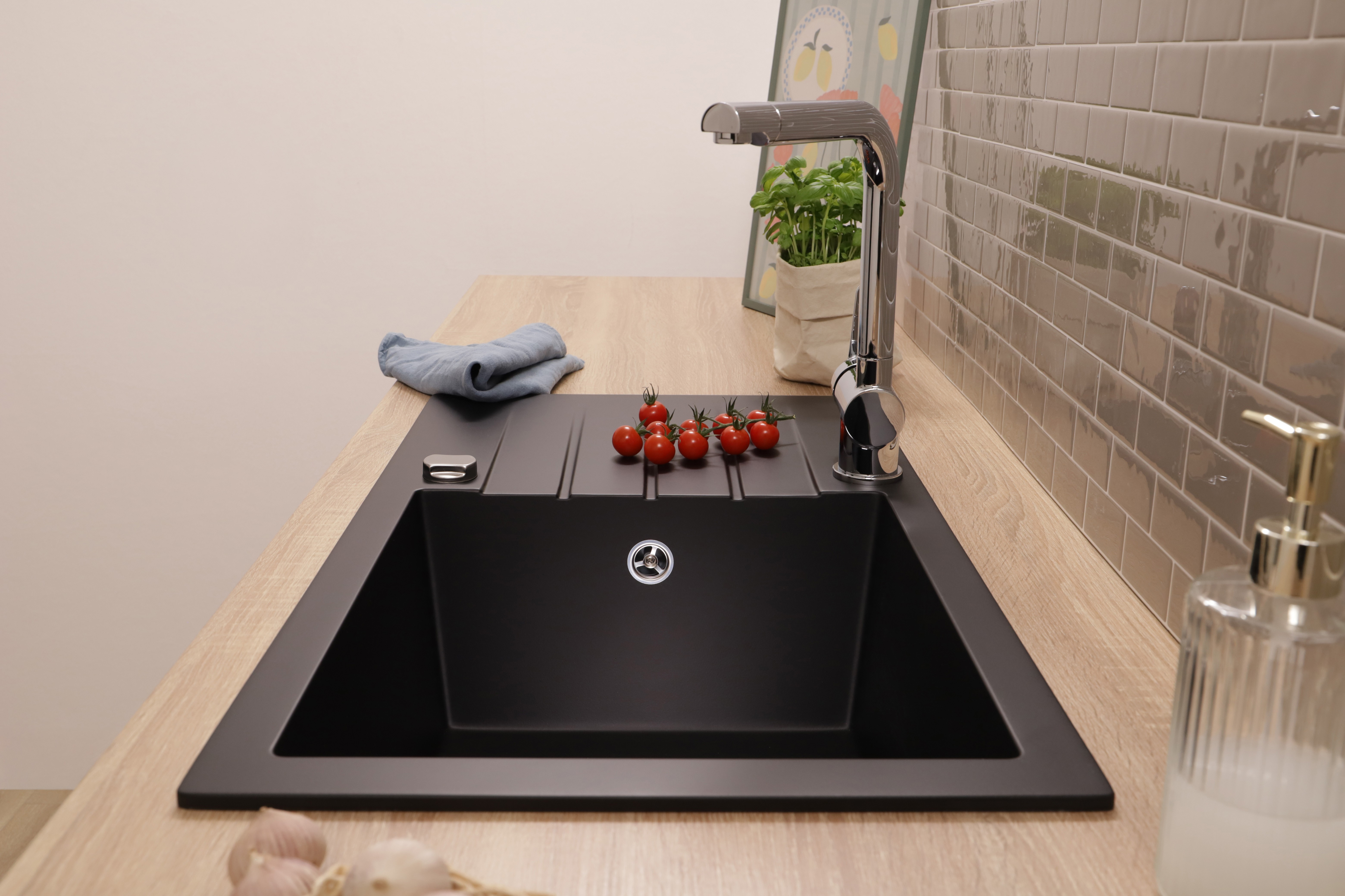 Eine schwarze Küchenspüle mit Chromarmatur auf einer Holzarbeitsplatte, mit Kirschtomaten und Kräutern.