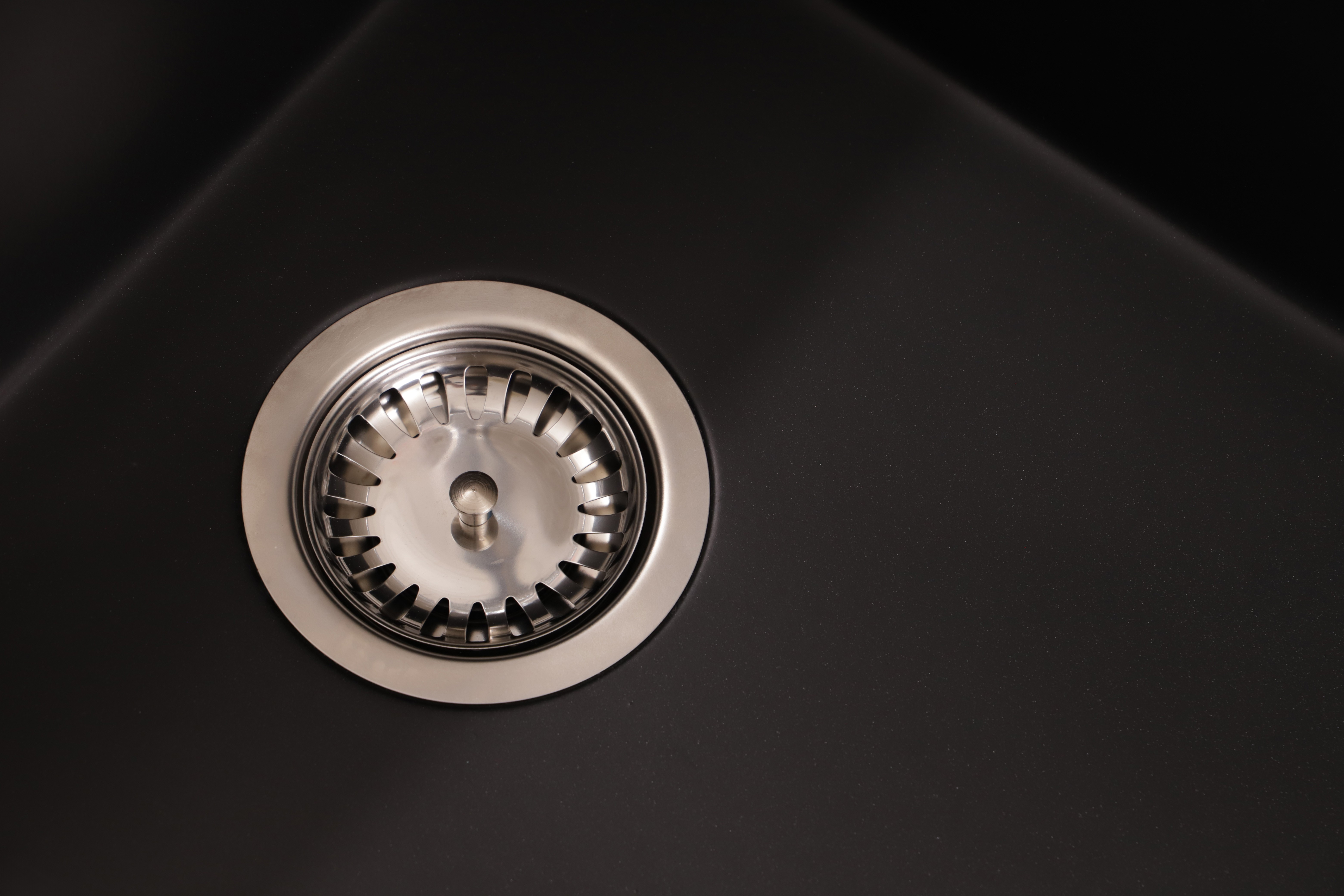 Ein silberner Metallsiebablauf befindet sich in einem schwarzen Küchenspülbecken.