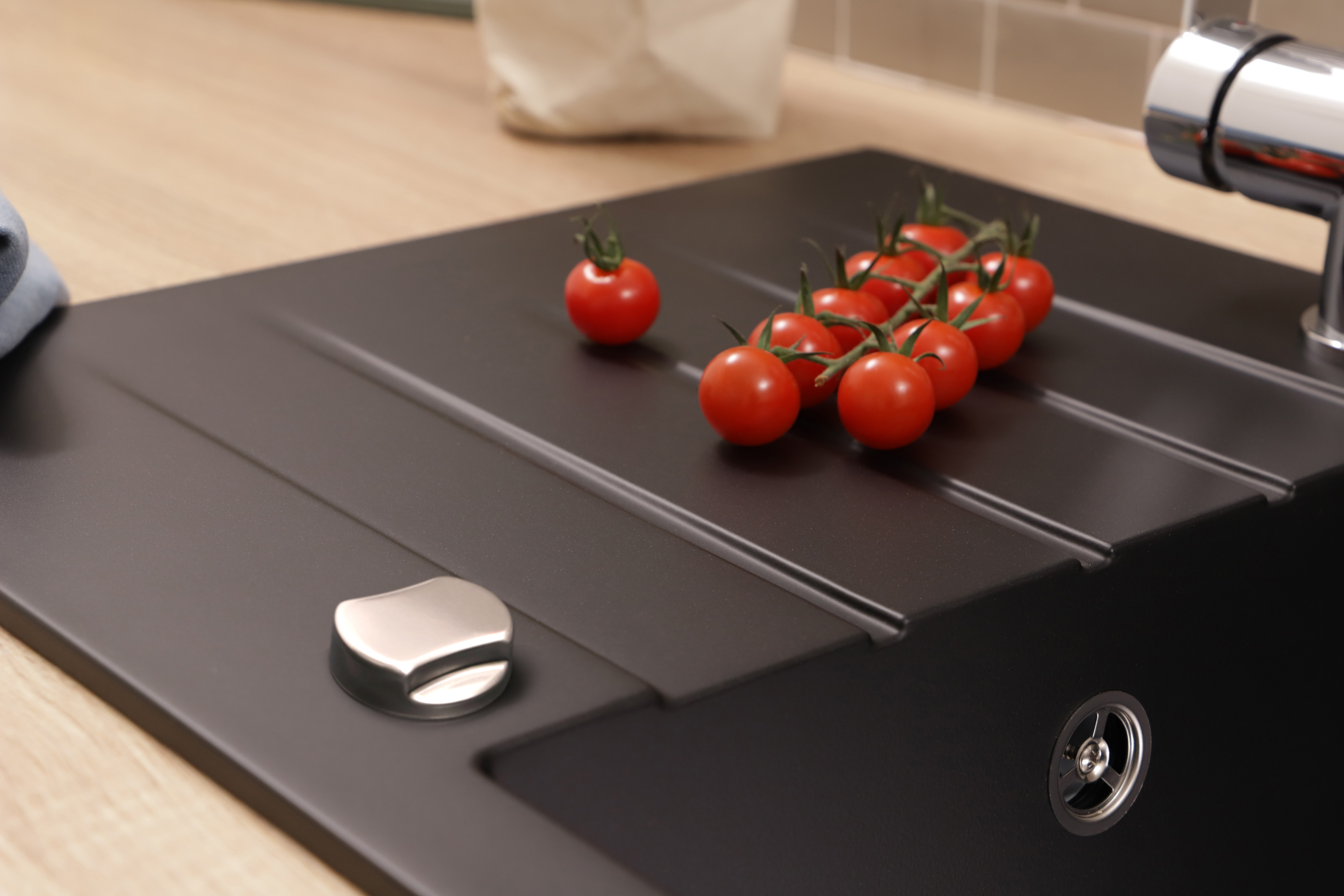 Eine Cluster reifer roter Kirschtomaten liegt auf einer modernen schwarzen Küchenspüle neben einem Chromwasserhahn.