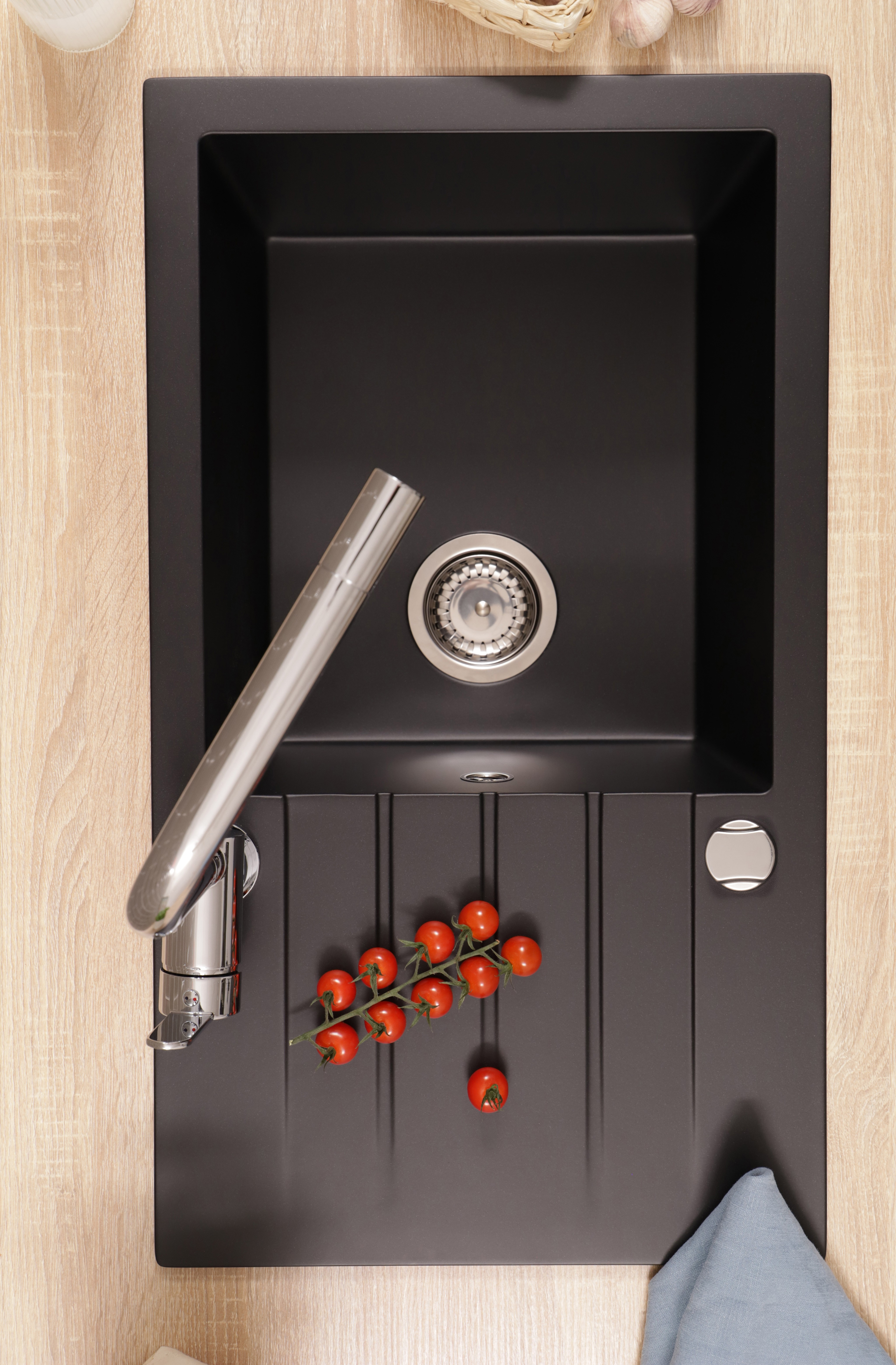 Ein schwarzes Spülbecken mit Chromarmatur und Tomaten auf der Abtropffläche, in einer Holzküche.