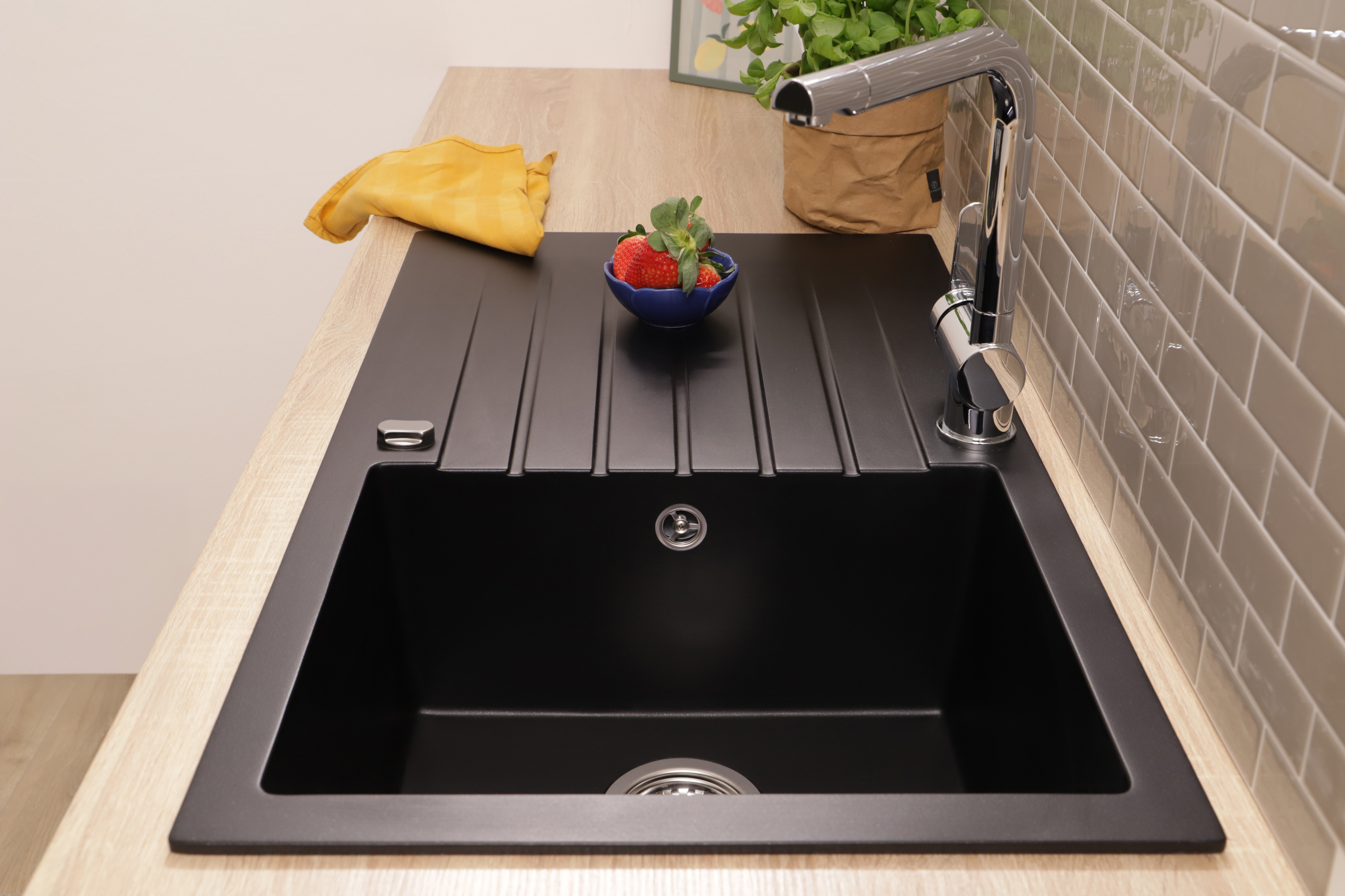 Eine schwarze Küchenspüle mit Chromarmatur auf einer Holzarbeitsplatte und Erdbeeren in einer kleinen Schüssel.