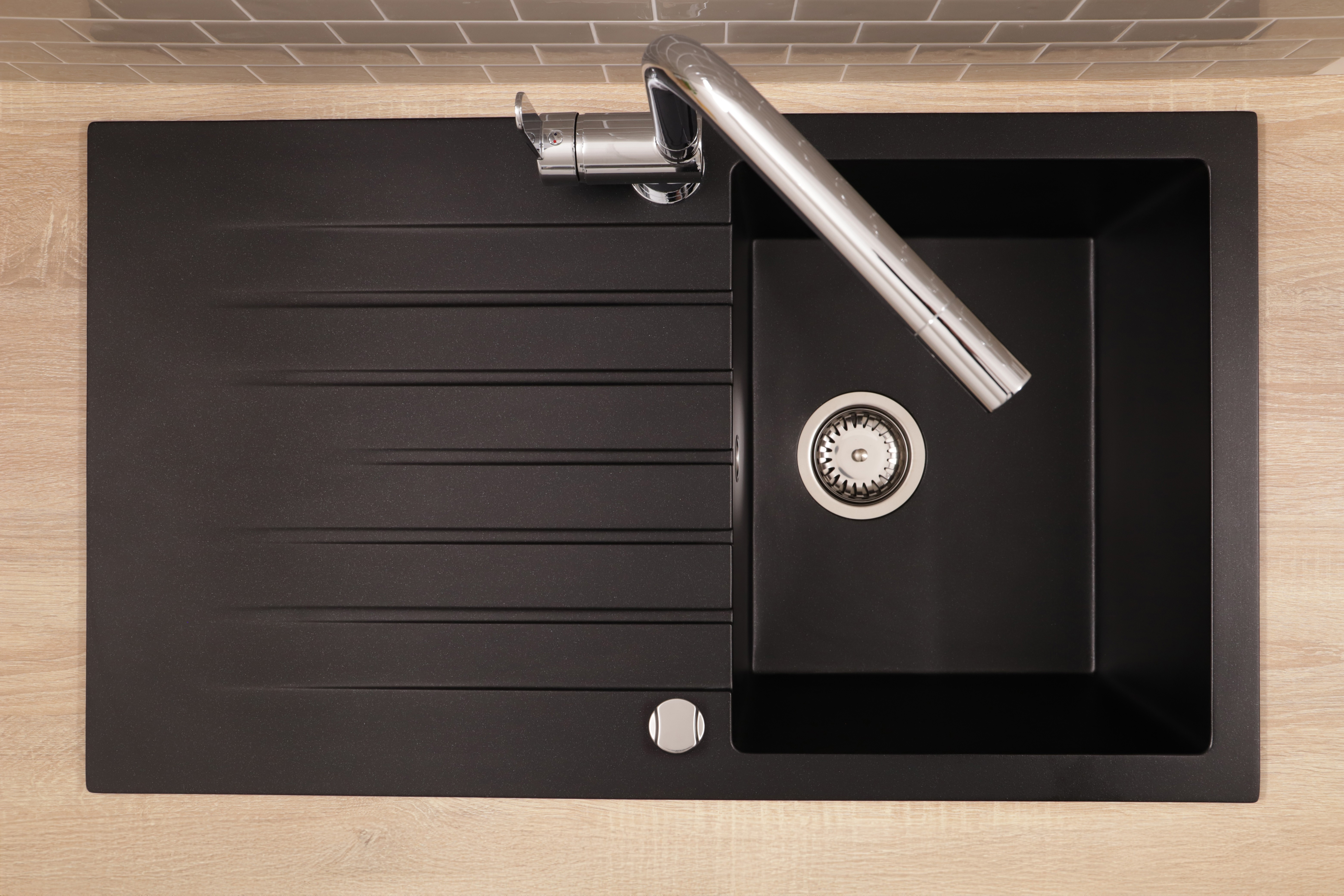 Eine schwarze Küchenspüle mit integriertem Abtropffläche und einem modernen verchromten Wasserhahn auf einer Arbeitsplatte.