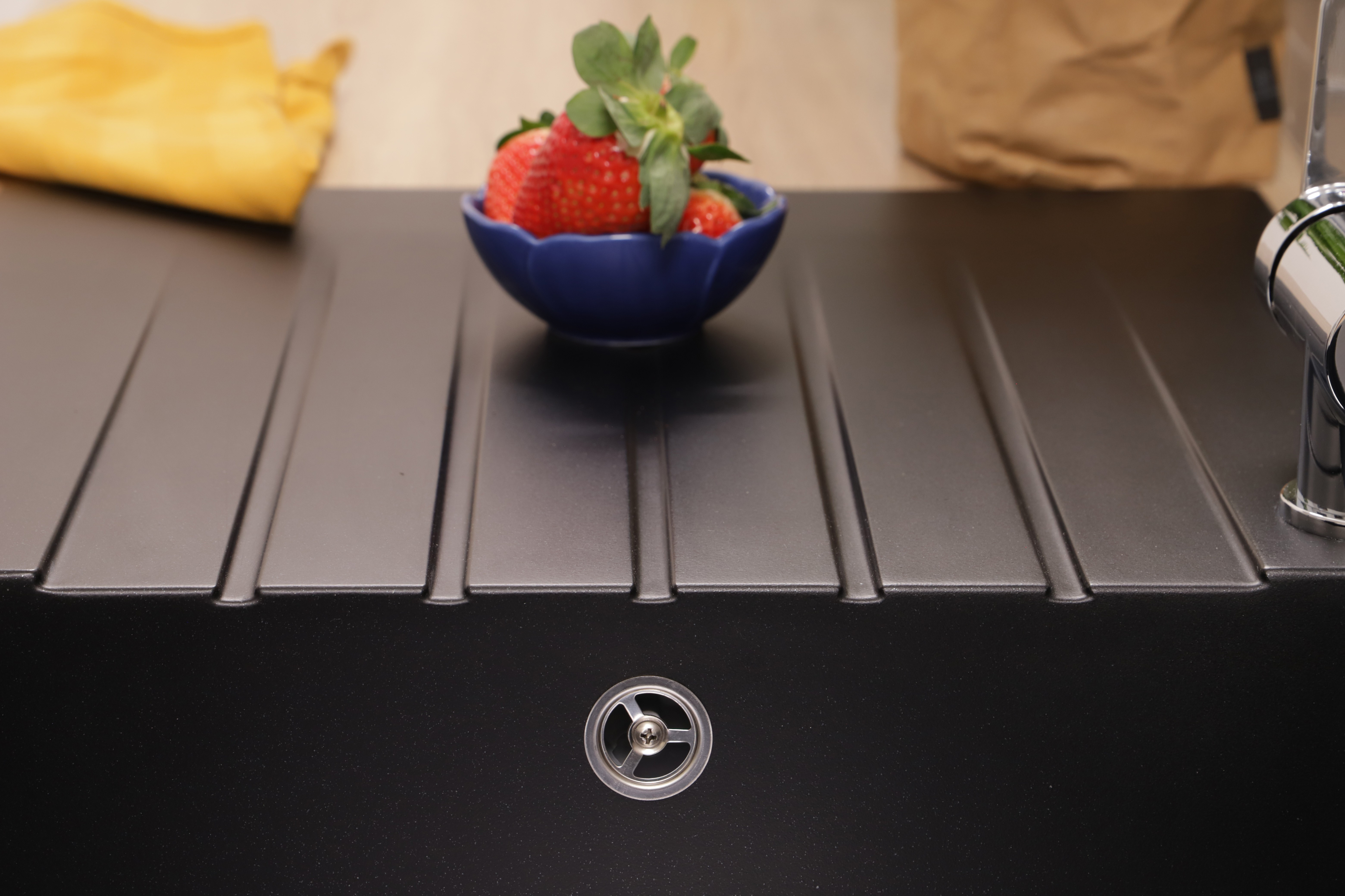 Eine blaue Schüssel mit frischen Erdbeeren steht auf einer modernen schwarzen Spüle.