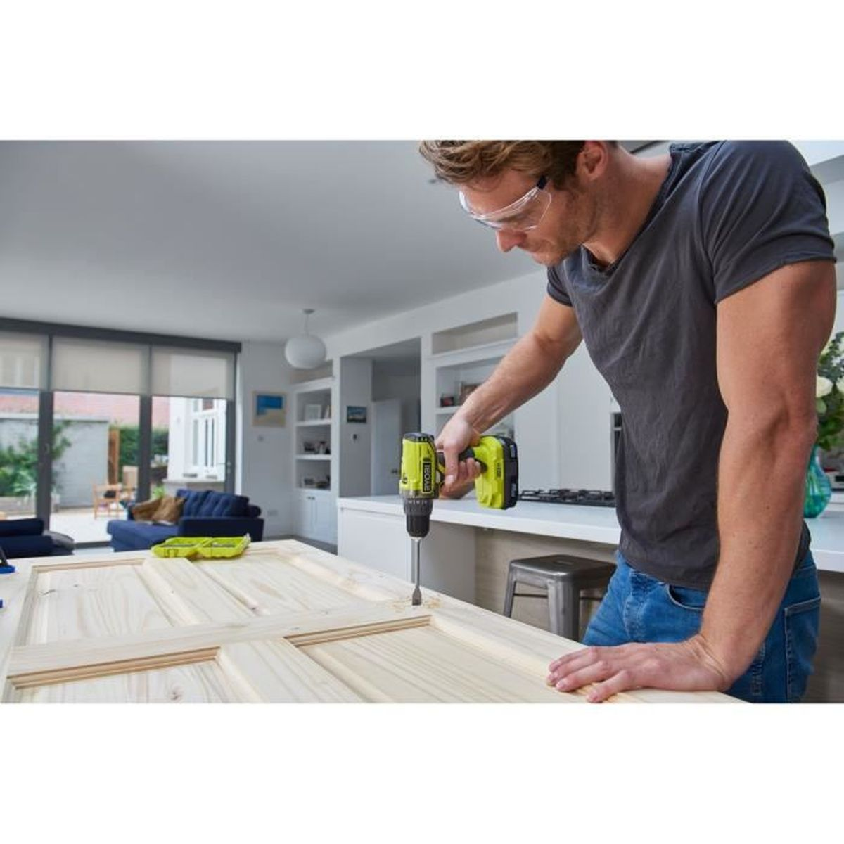 Un uomo con occhiali di protezione fora un pannello di legno in una cucina moderna.