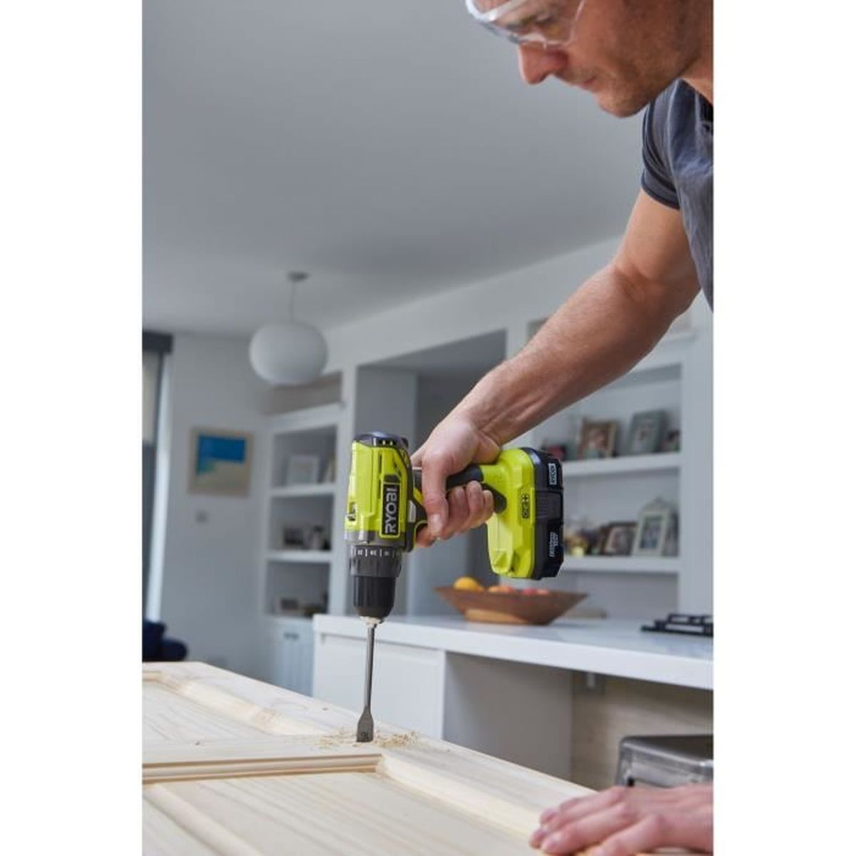 Uomo fora una porta di legno con un trapano a batteria giallo in casa.