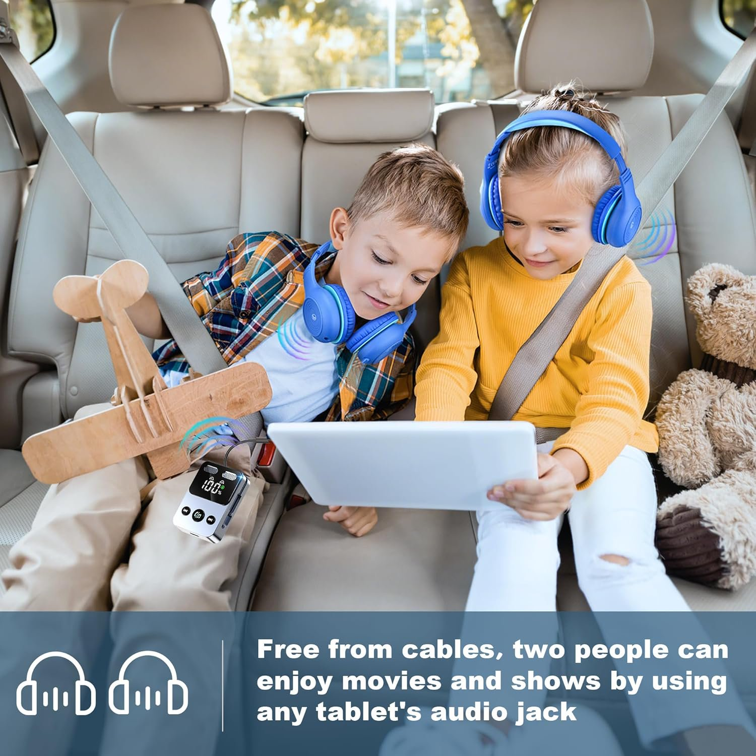 Zwei Kinder sitzen im Auto, tragen blaue Kopfhörer und schauen gemeinsam auf ein weißes Tablet.